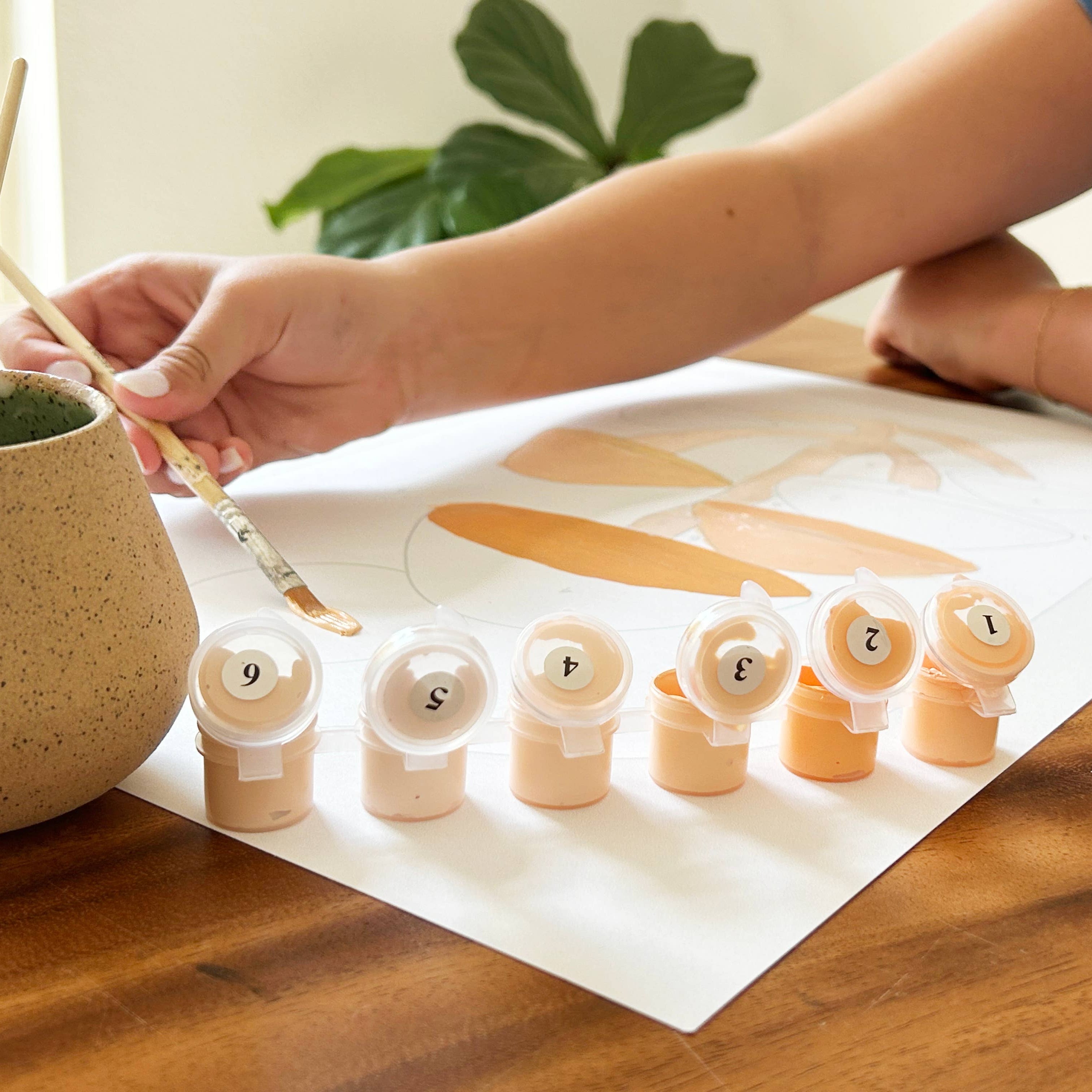 Person painting wooden numbers with a brush on a wooden table.
