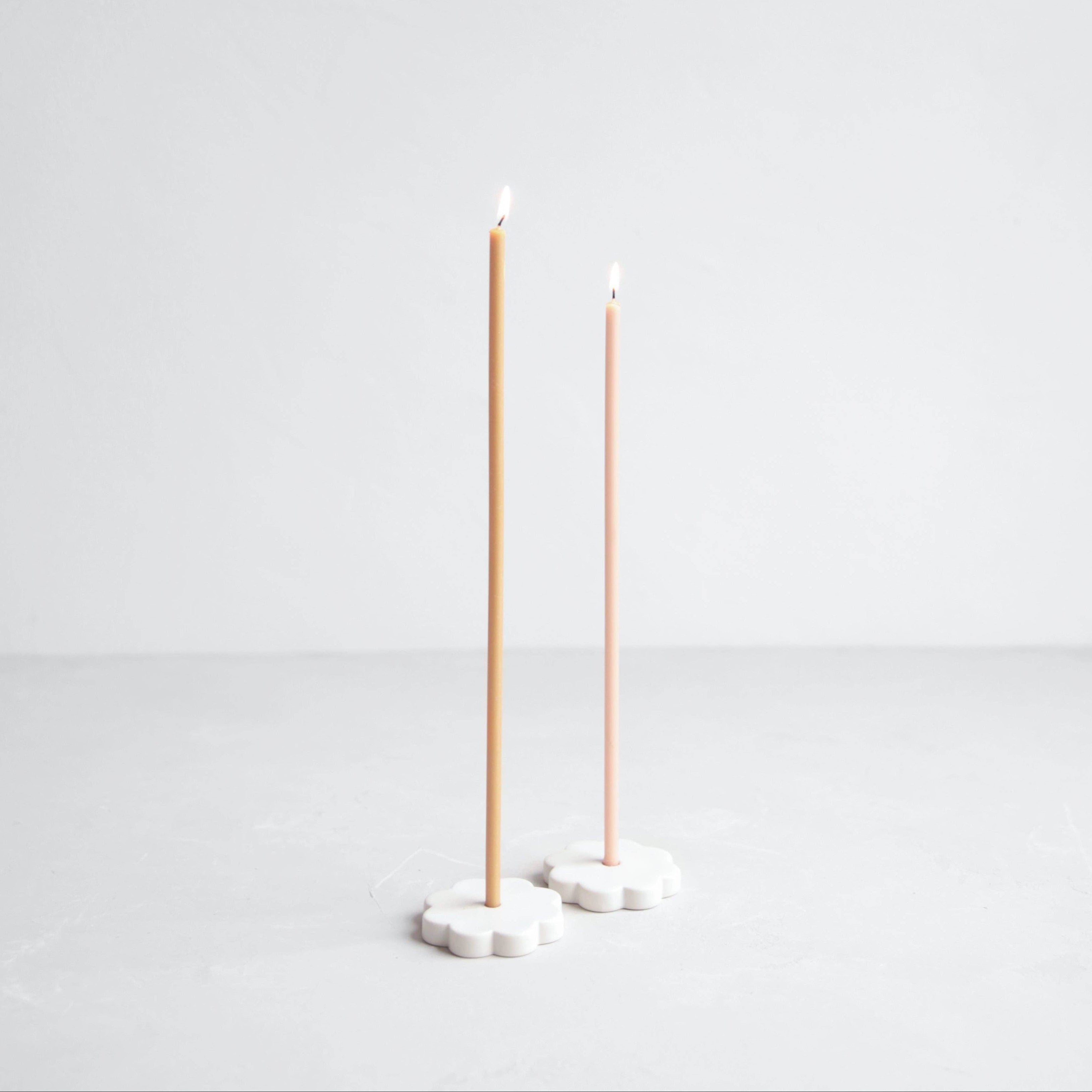 Two tall, thin candles on white stands against a light gray background