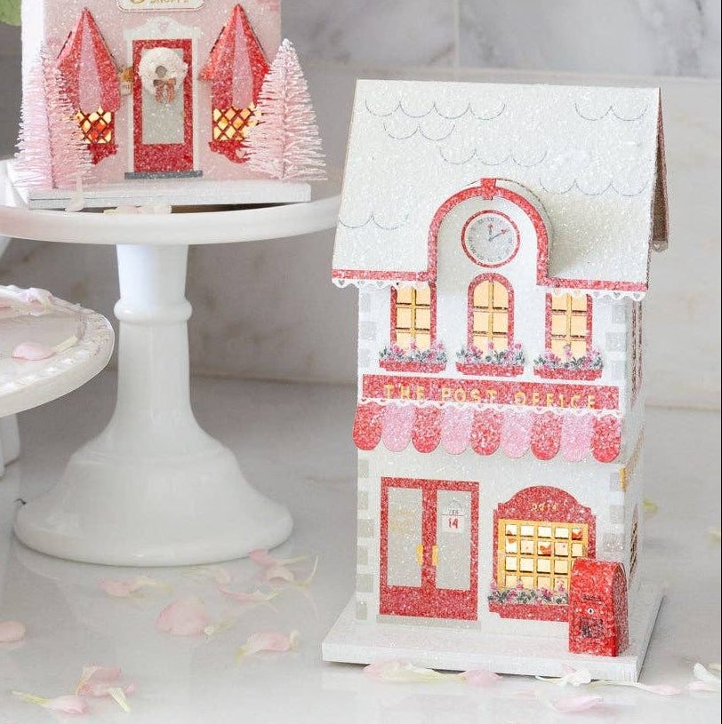 Welcome to the cutest corner of your Valentine's Day celebration! This charming Post Office paper house brings nostalgic magic to your village display. Perfect for creating an enchanting holiday scene, this detailed piece adds character and whimsy to any festive setup. Whether you're building a complete village display or adding a special touch to your party décor, this post office is perfect for your shelf.

Details:

Red, pink, and cream post office
Post office is 4" wide x 3.5" deep x 6.5" tall