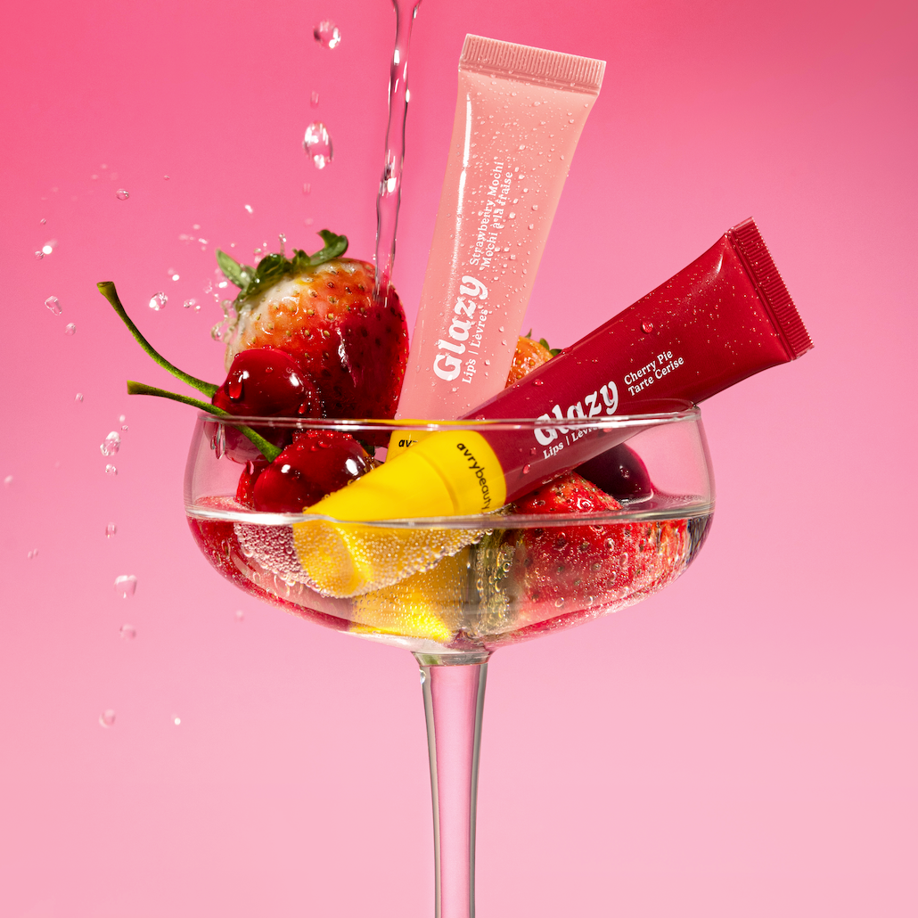 Two tubes of Glossy products in a glass with strawberries and cherries on a pink background