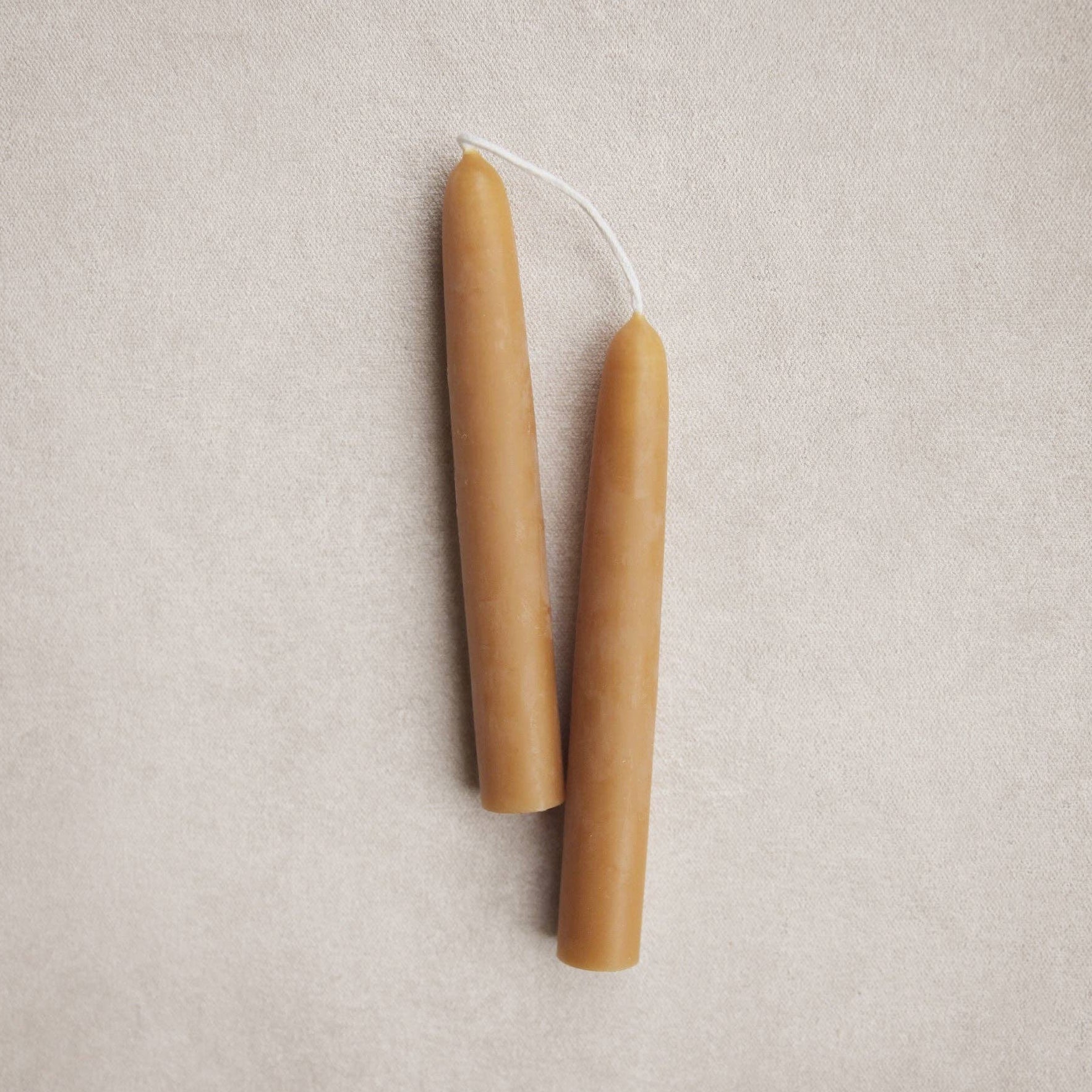 Two beige candles on a light gray background. Ochre