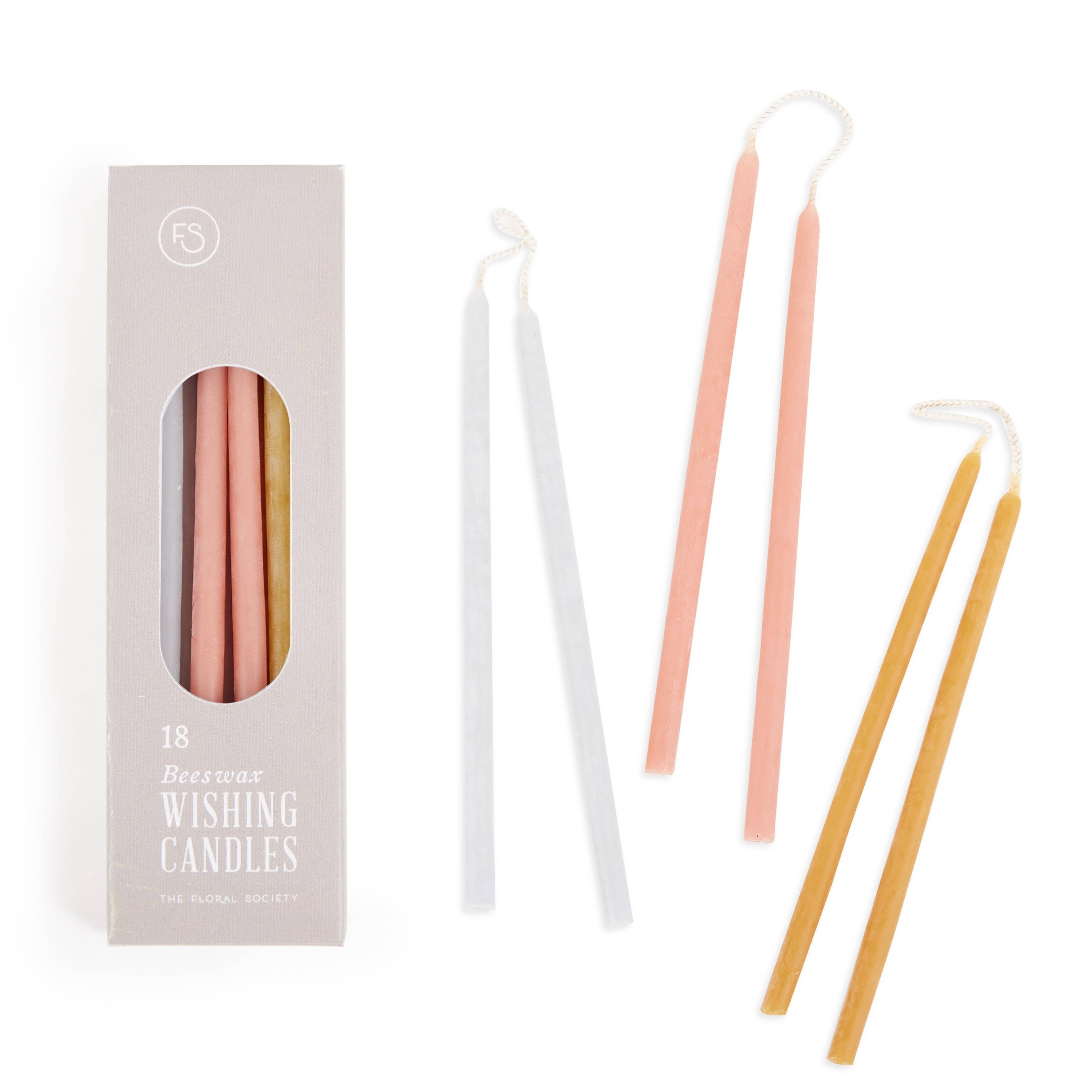 Set of three wishing candles in pink, white, and yellow with a packaging box on a white background.