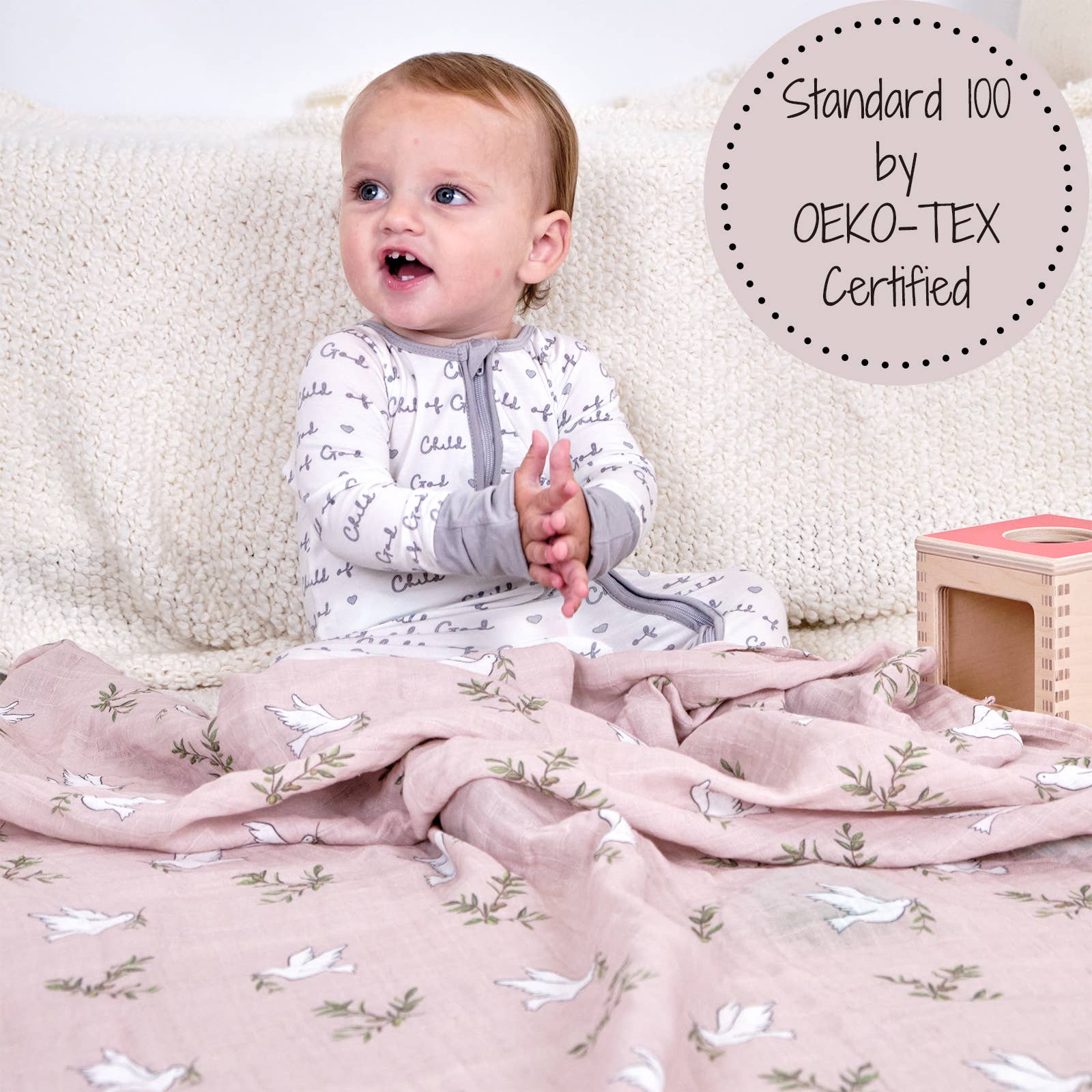 Baby sitting on a soft surface with a pink blanket featuring white bird patterns, surrounded by educational toys.