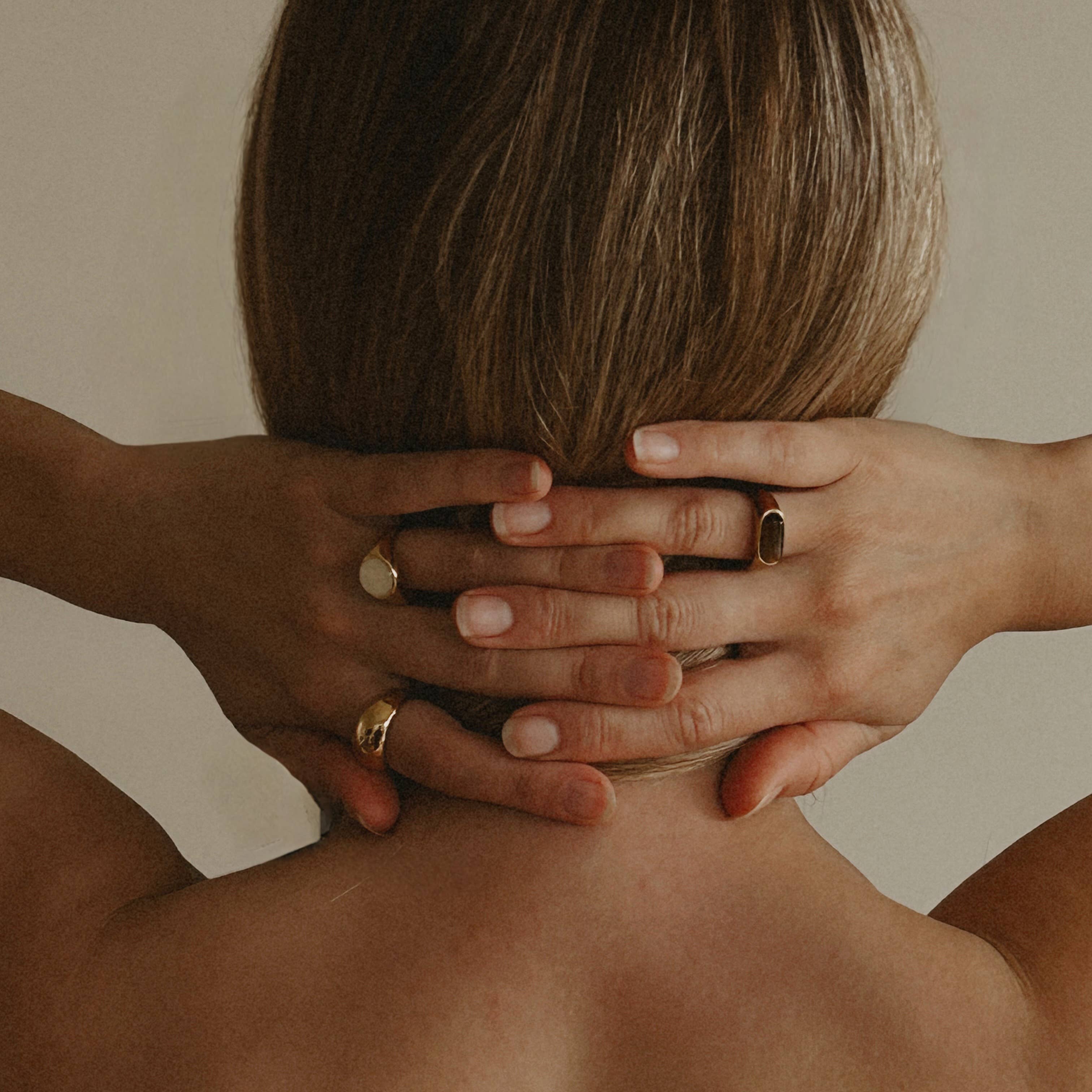 Two hands with gold rings on a neutral background