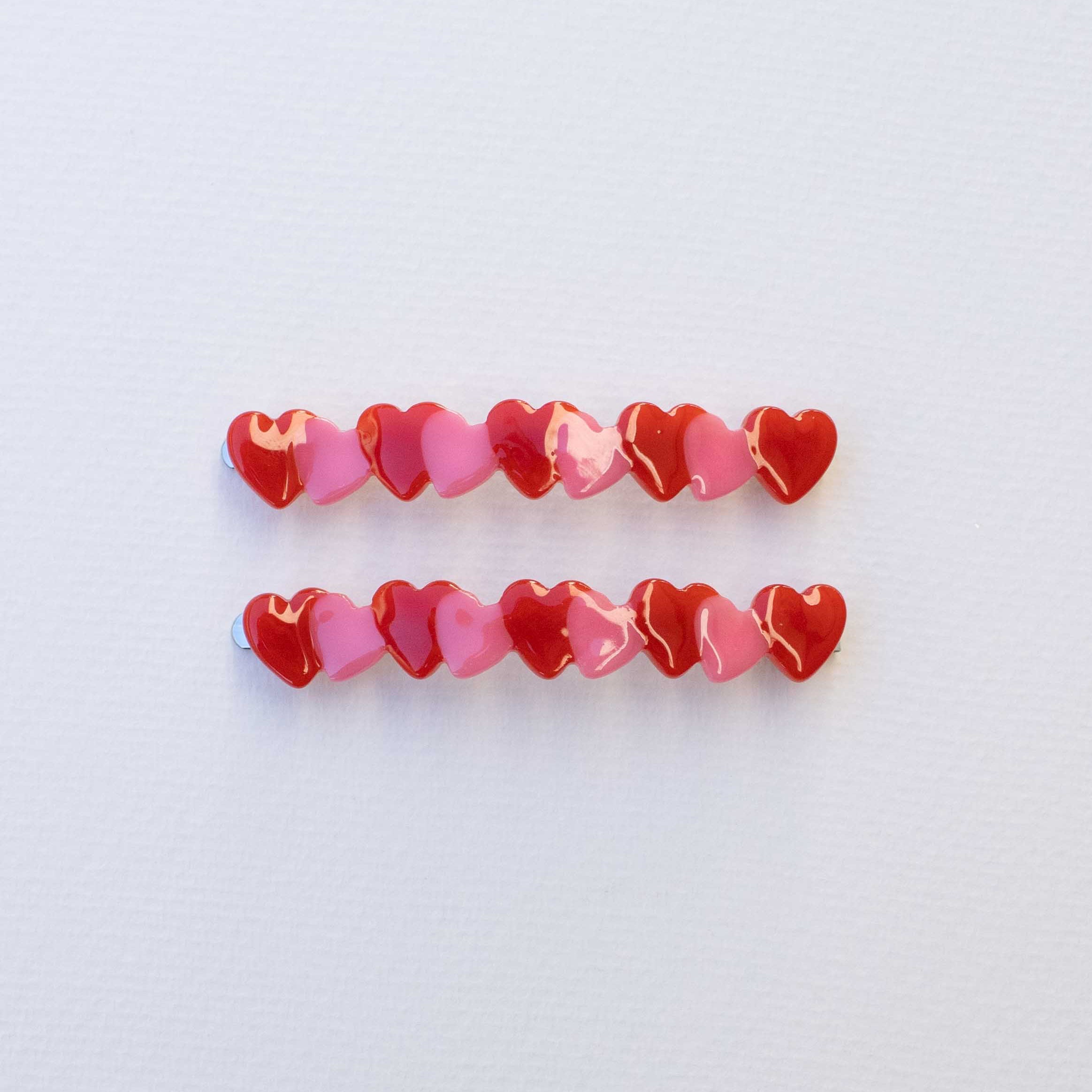 Hold onto your style with this charming hair pin set of two. Each sleek pin is adorned with red and pink delicate hearts running along its length, adding a sweet romantic touch to any hairstyle. Whether you're securing an updo, creating texture, or simply keeping strands in place throughout the day, these pins blend functionality with understated elegance. Perfect for everyday wear or special occasions, this set gives you versatile styling options while celebrating those little details that make you smile.