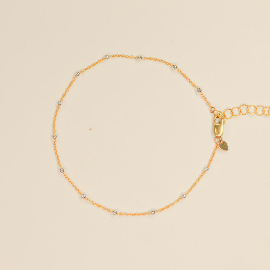 Delicate gold bracelet with tiny silver beads dotting the length intermittently. Pictured on an off white background.
