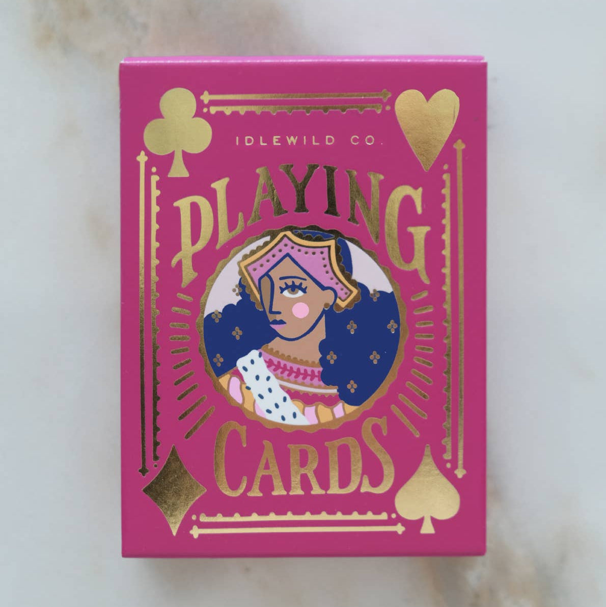 Pink playing card box with gold text and illustrations on a marble surface
