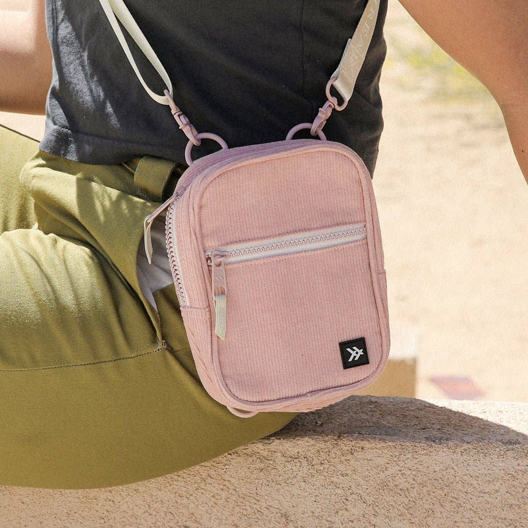 Pink crossbody bag worn by a person sitting on a sandy surface