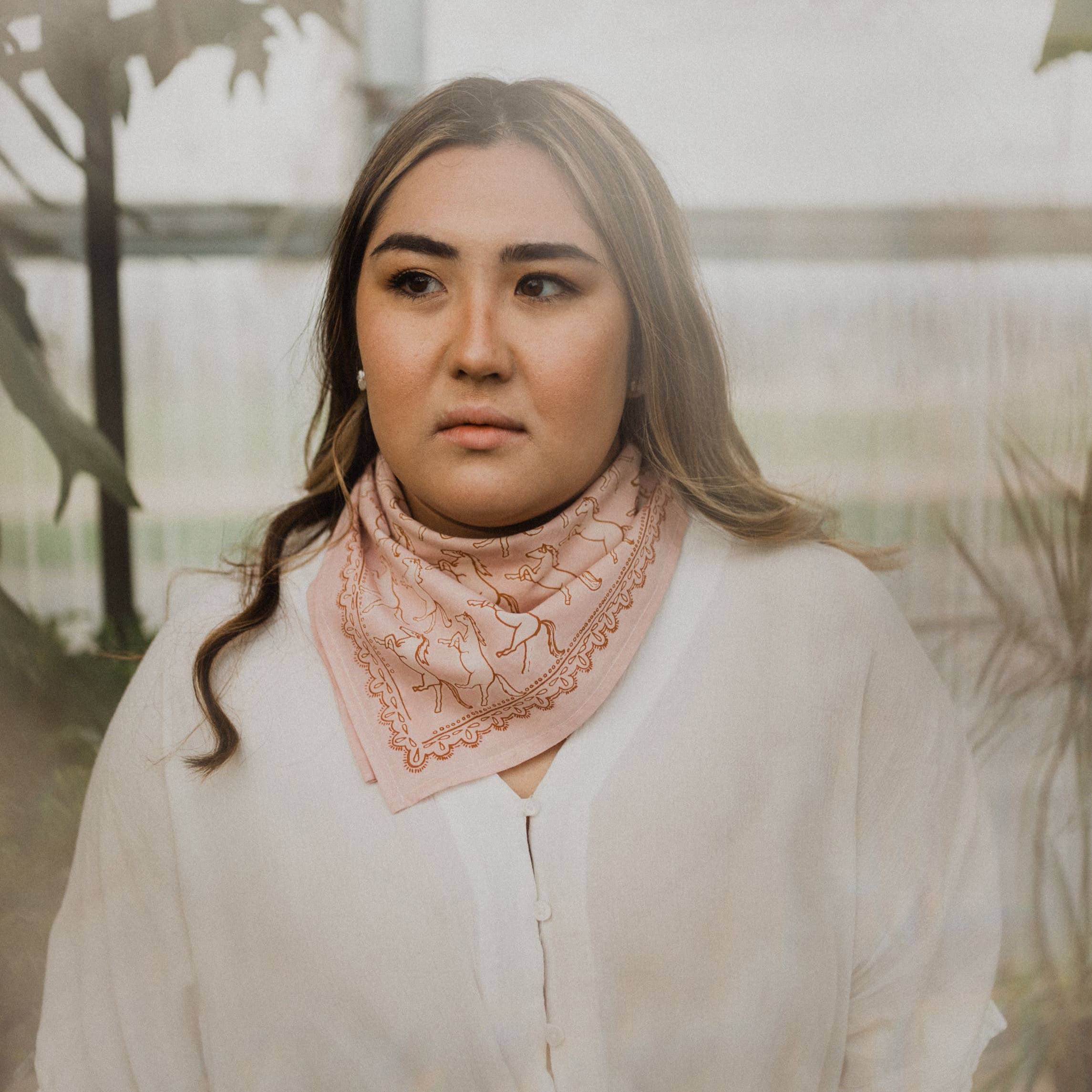 Woman wearing a pink scarf with a blurred outdoor background