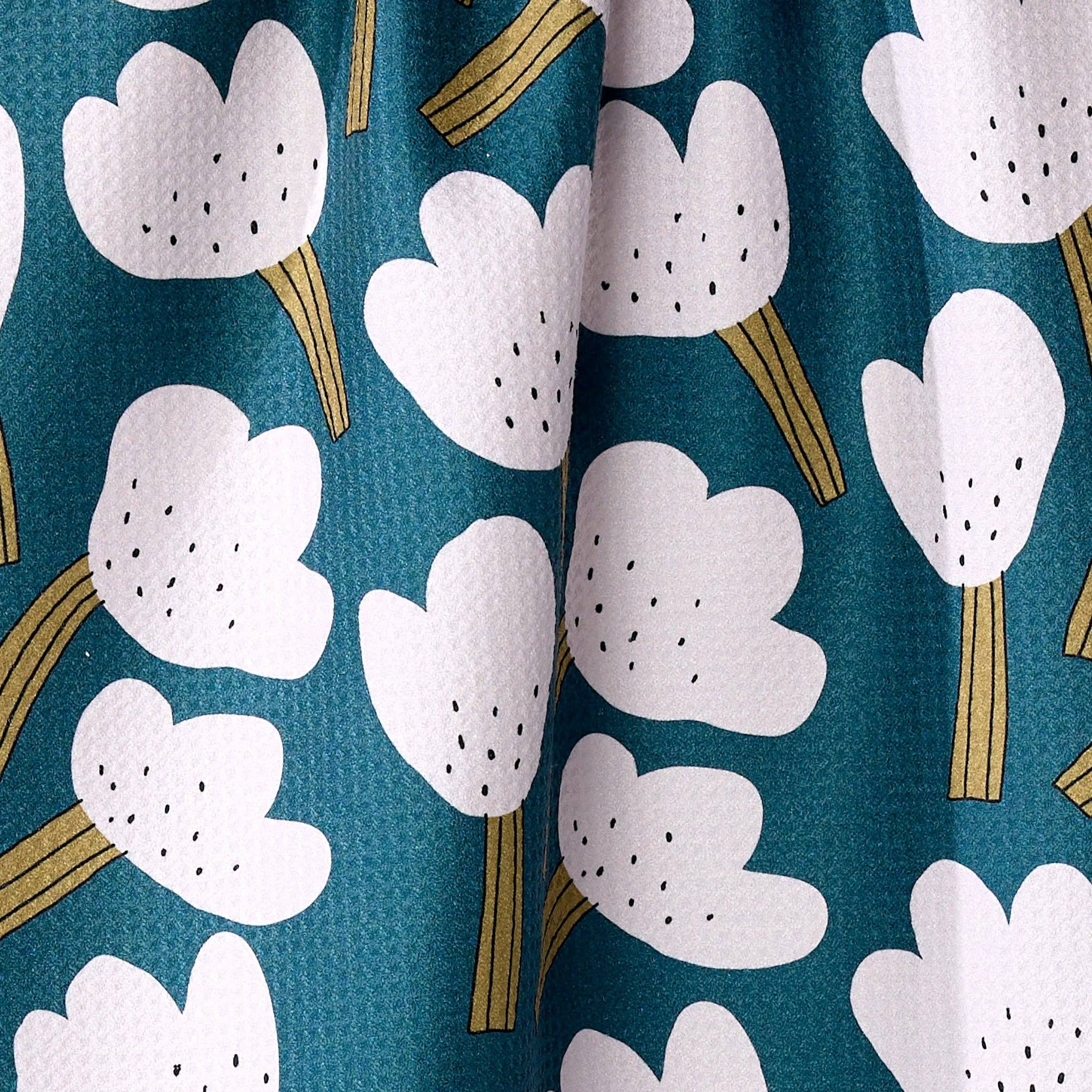 white  tea towel  floral pattern on a teal background hanging against a plain wall.
