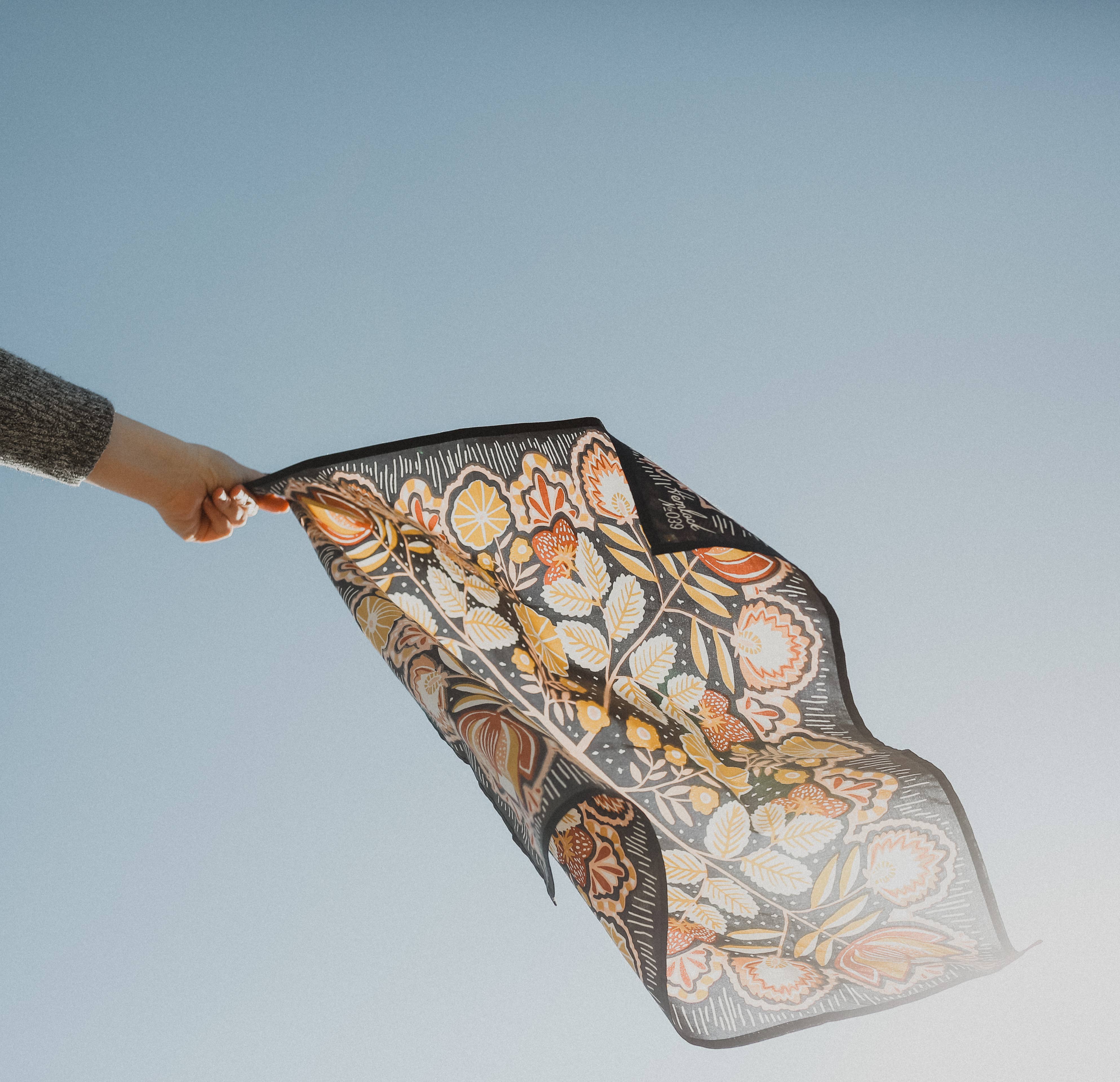 Person holding a floral-patterned scarf against a clear blue sky
