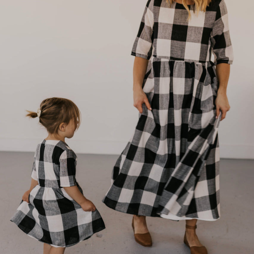 Now you and your mini can match in this ROOLEE classic! This dress features a timeless buffalo plaid that is bold, sophisticated and the perfect style for every occasion. Breathable, woven material is paired with hip pockets, half sleeves, a full lining, a gathered waist, and a flowing skirt. The Mini Maddie Buffalo Plaid Dress is adorable, versatile, and sure to be your daughter's favorite dress! Black Plaid