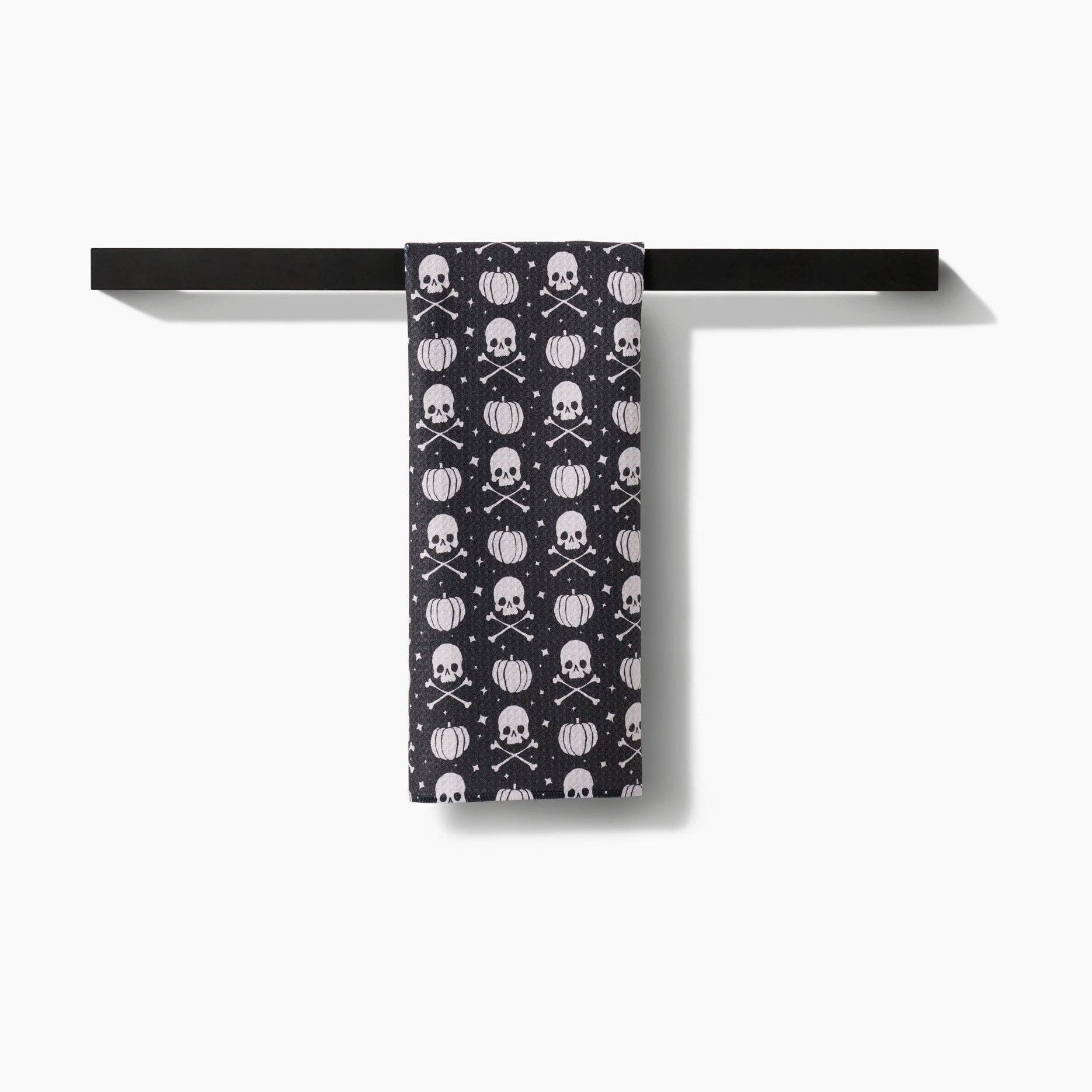 Black towel with skull and crossbones pattern hanging on a black rack against a white background