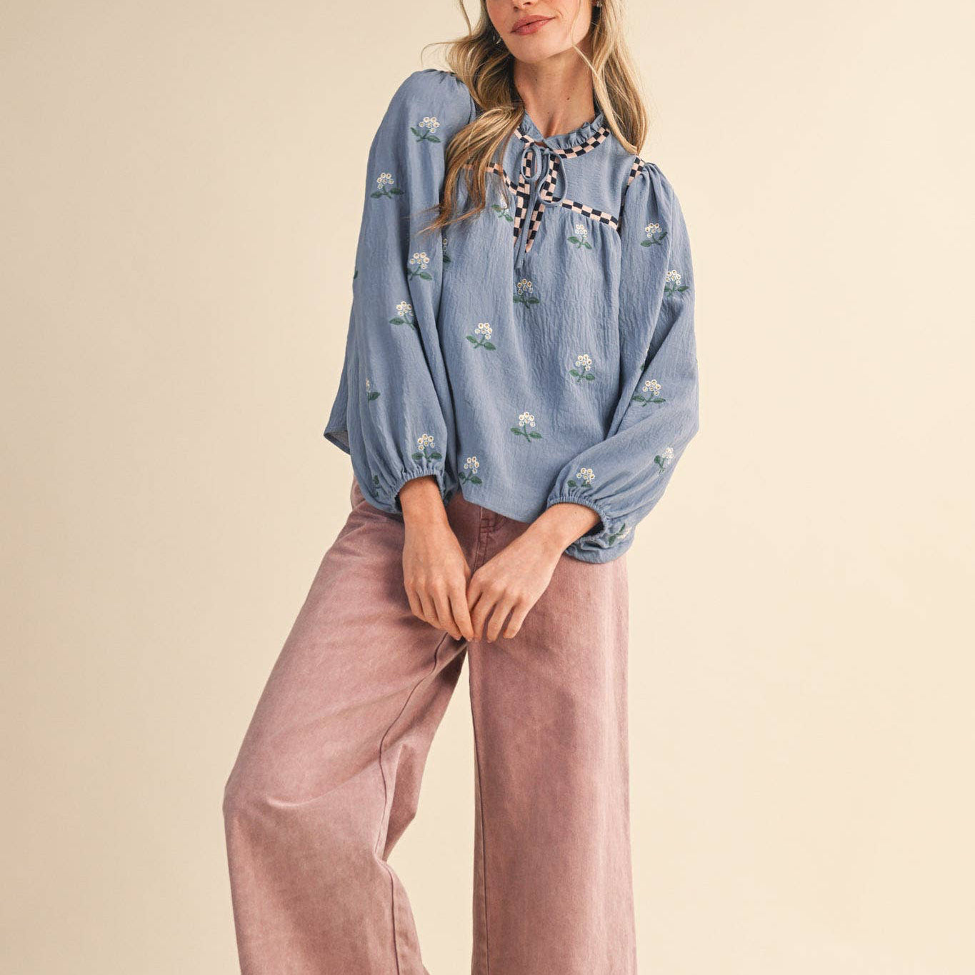 Embrace effortless charm with this enchanting floral embroidered babydoll top in soft dusty blue. The delicate all-over floral embroidery paired with checkered details on the neckline and yoke creates a romantic, thoughtfully designed piece that celebrates feminine style. The ruffled neckline features a sweet keyhole opening with tying detail, while long balloon sleeves with elastic cuffs offer a flattering, comfortable fit. Fully lined for confidence and ease.
