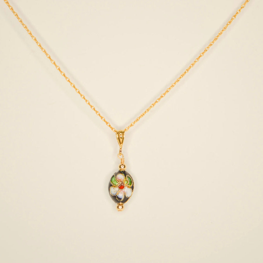 Delicate gold chain with a oval black bead that has a pink painted flower. Pictured on an off white background.