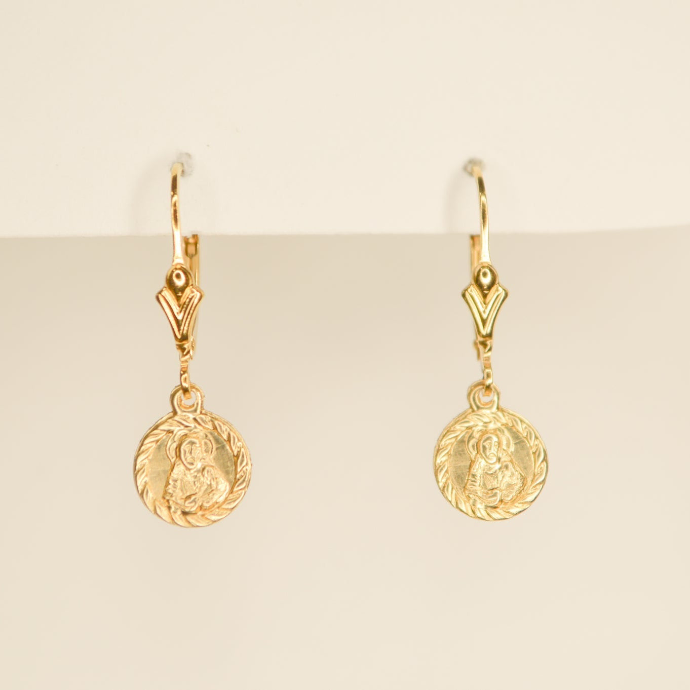 Gold leverback earrings with small circle token dangles on a cream background. 