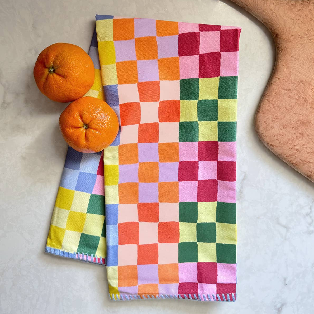 Colorful checkered towels with oranges and a wooden cutting board on a light surface
