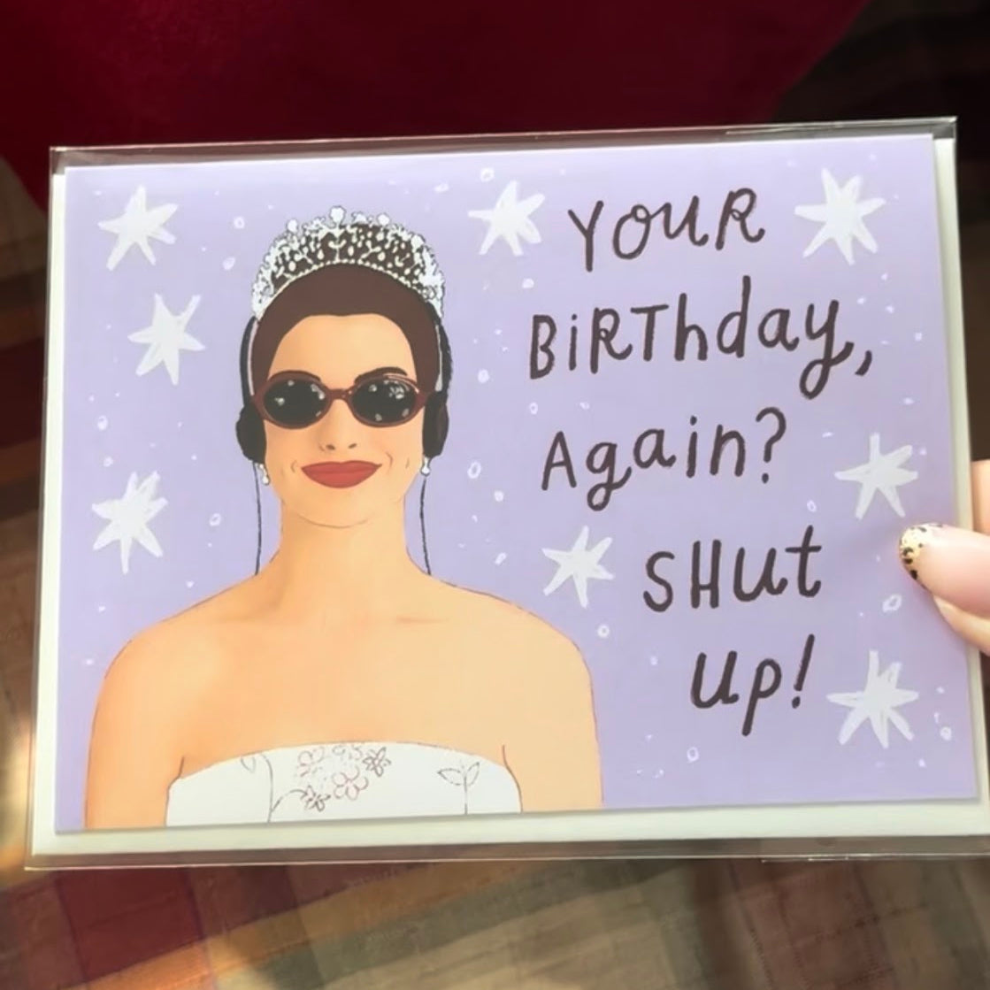Birthday card with illustration of a woman wearing sunglasses and a tiara, text 'Your Birthday, Again? Shut up!' on a purple background.