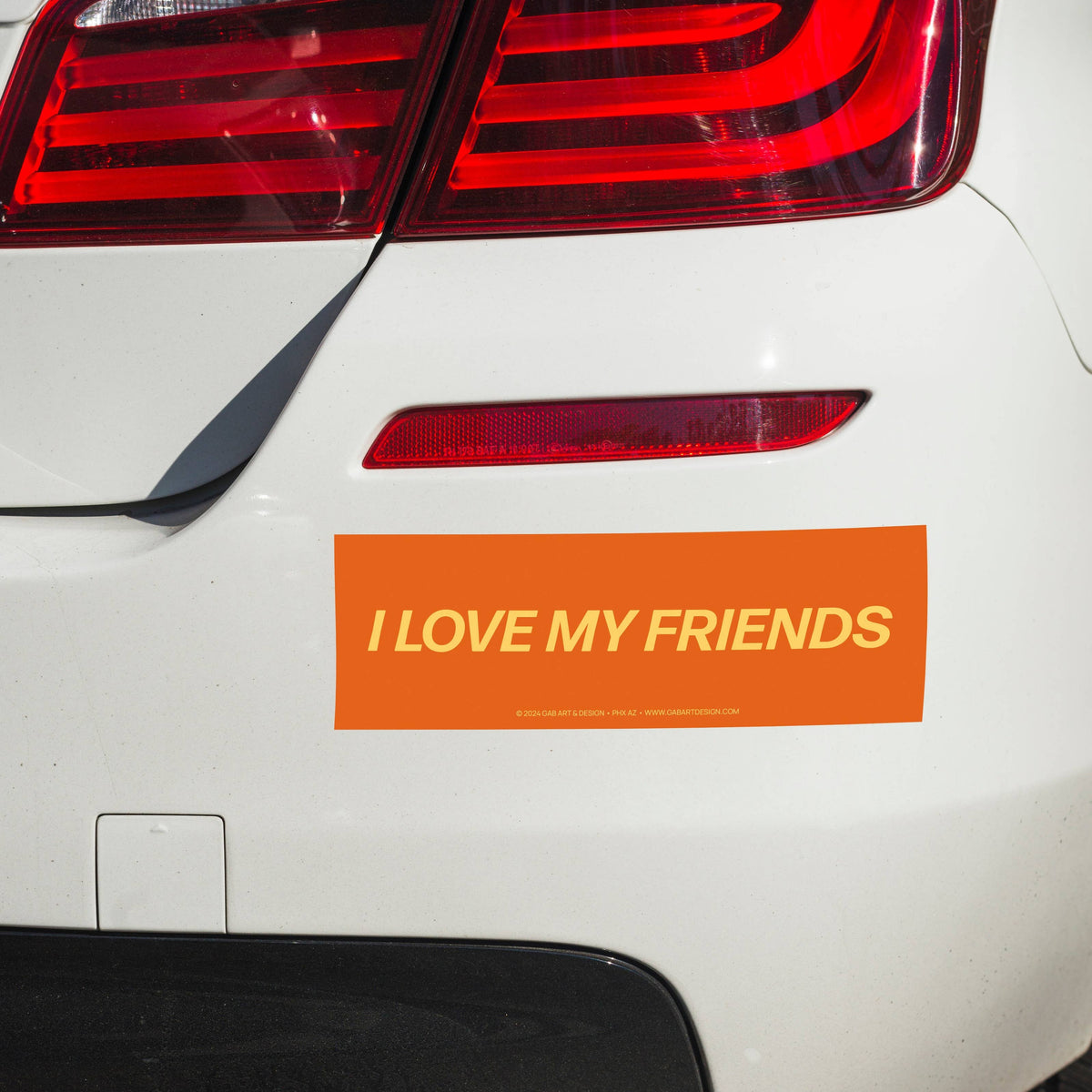 Car tail light with 'I LOVE MY FRIENDS' bumper sticker on a white car.