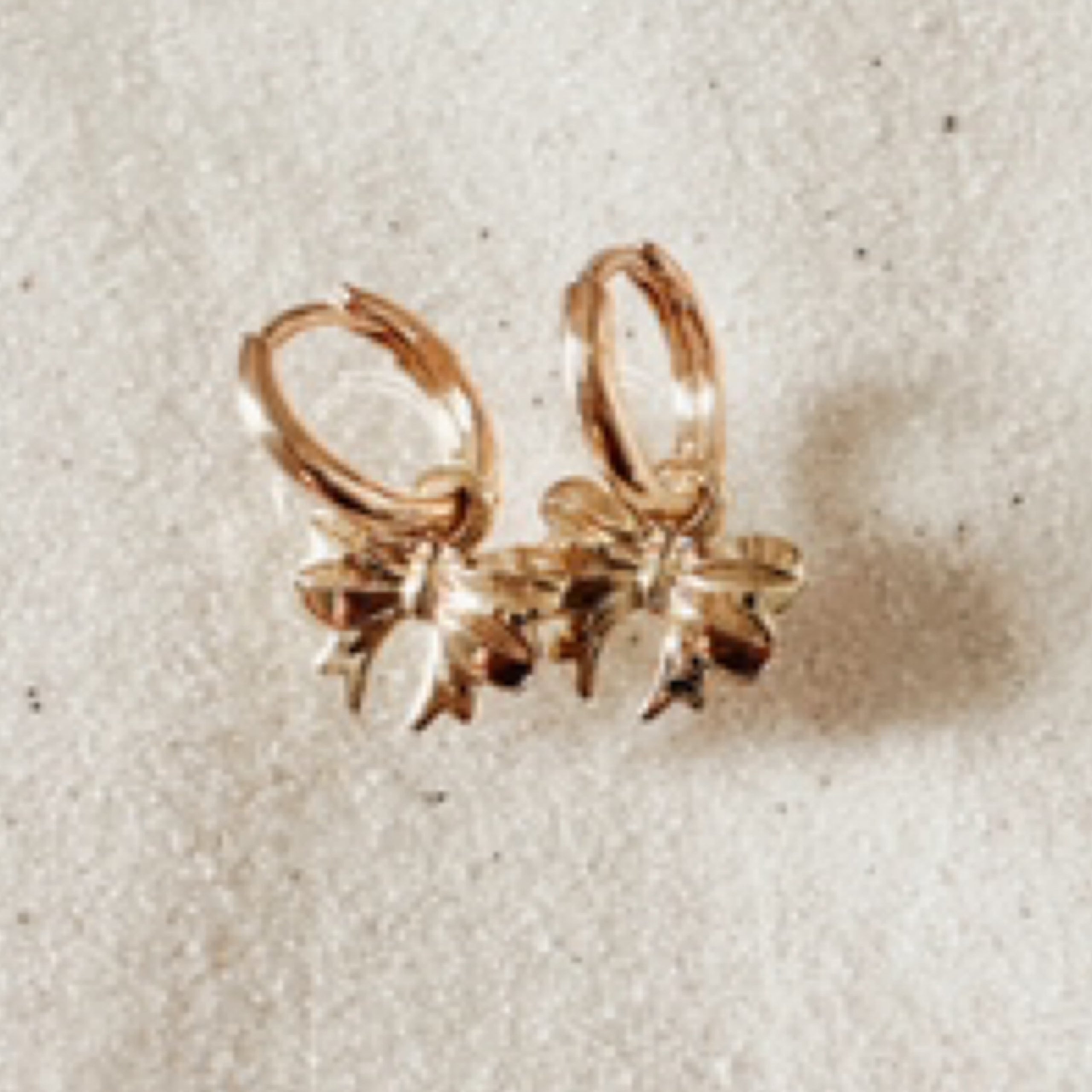 Gold huggies with a detailed bow dangle. Pictured against white sand.