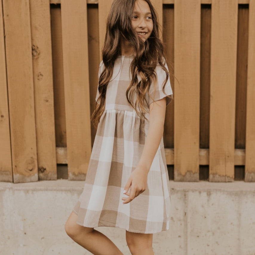Now you and your mini can match in this ROOLEE classic! This dress features a timeless buffalo plaid that is bold, sophisticated and the perfect style for every occasion. Breathable, woven material is paired with hip pockets, half sleeves, a full lining, a gathered waist, and a flowing skirt. The Mini Maddie Buffalo Plaid Dress is adorable, versatile, and sure to be your daughter's favorite dress! Tan Plaid