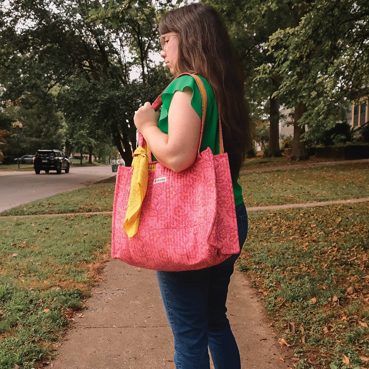 Person holding a pink tote bag with a yellow item on a sidewalk