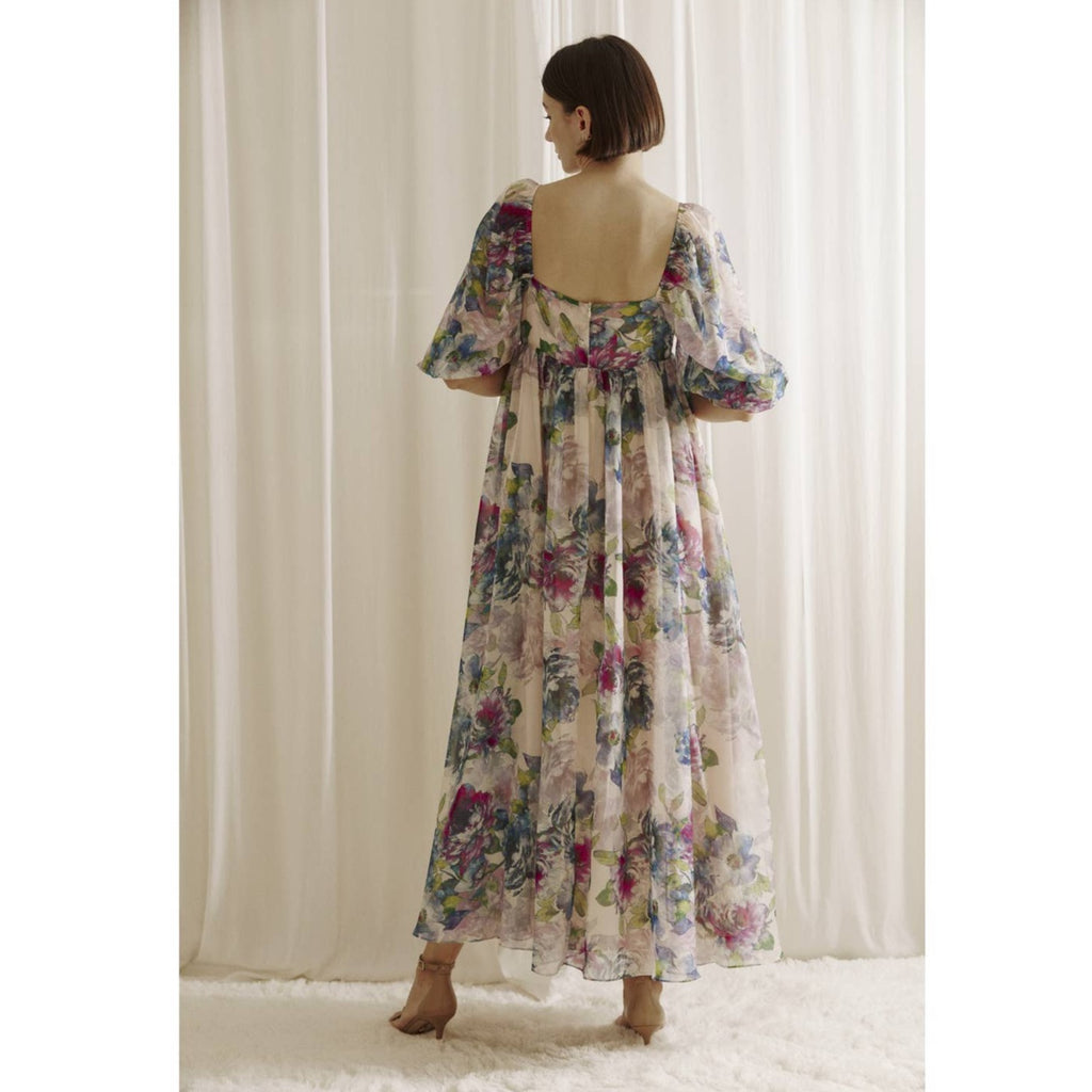 Multi-color watercolor floral print maxi baby doll dress. It shows a square neckline, 3/4 puffy sleeves, and bust darts. It also has an empire, gathered waist, back zipper, and flowy bottom.