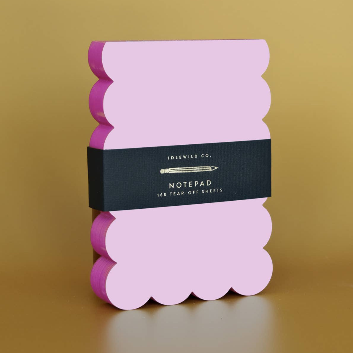 Pink notepad with scalloped edges and a black label on a gold background