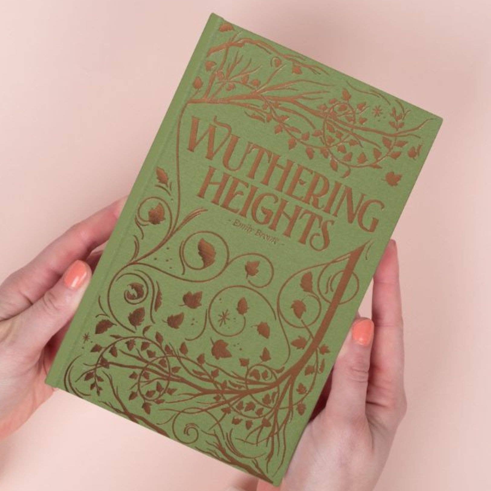 Green book titled 'Wuthering Heights' held by a person against a light pink background