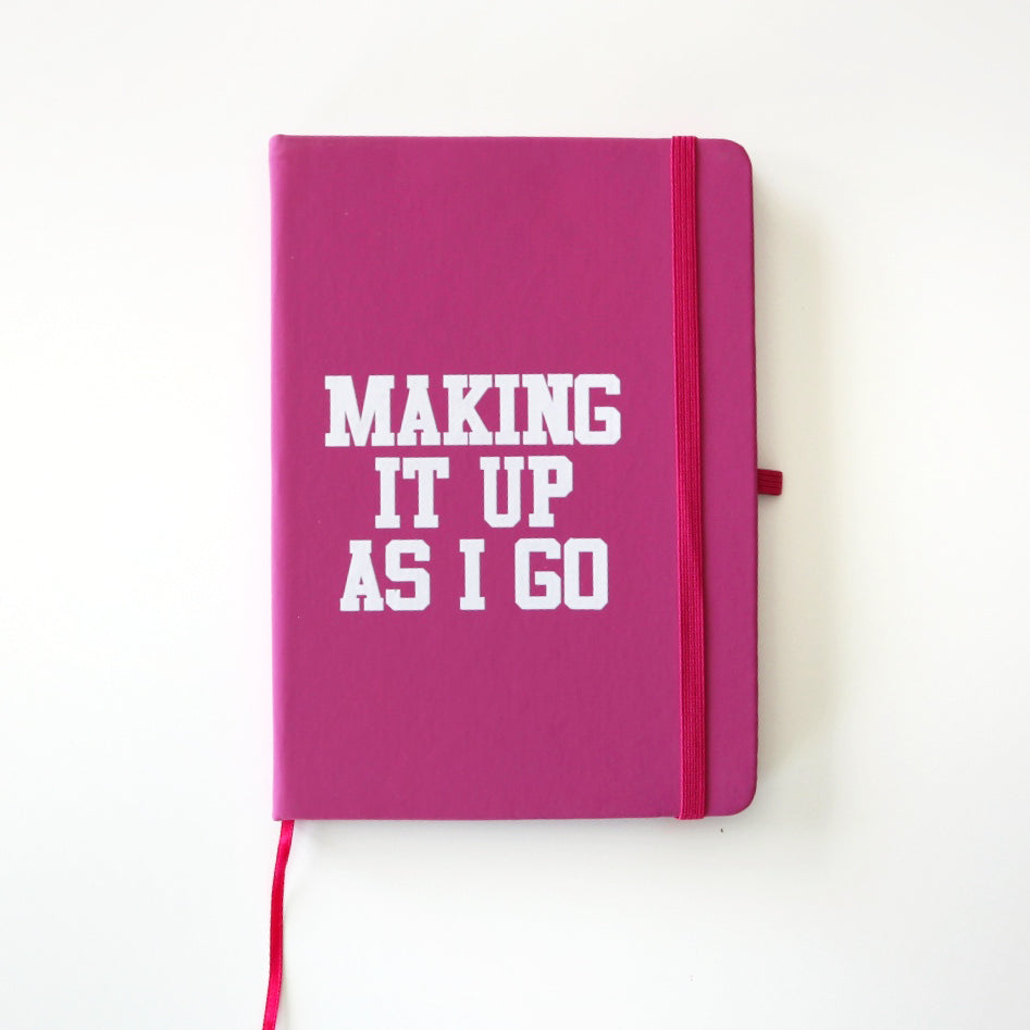 pink hardcover notebook reading "making it up as I go" in a white font