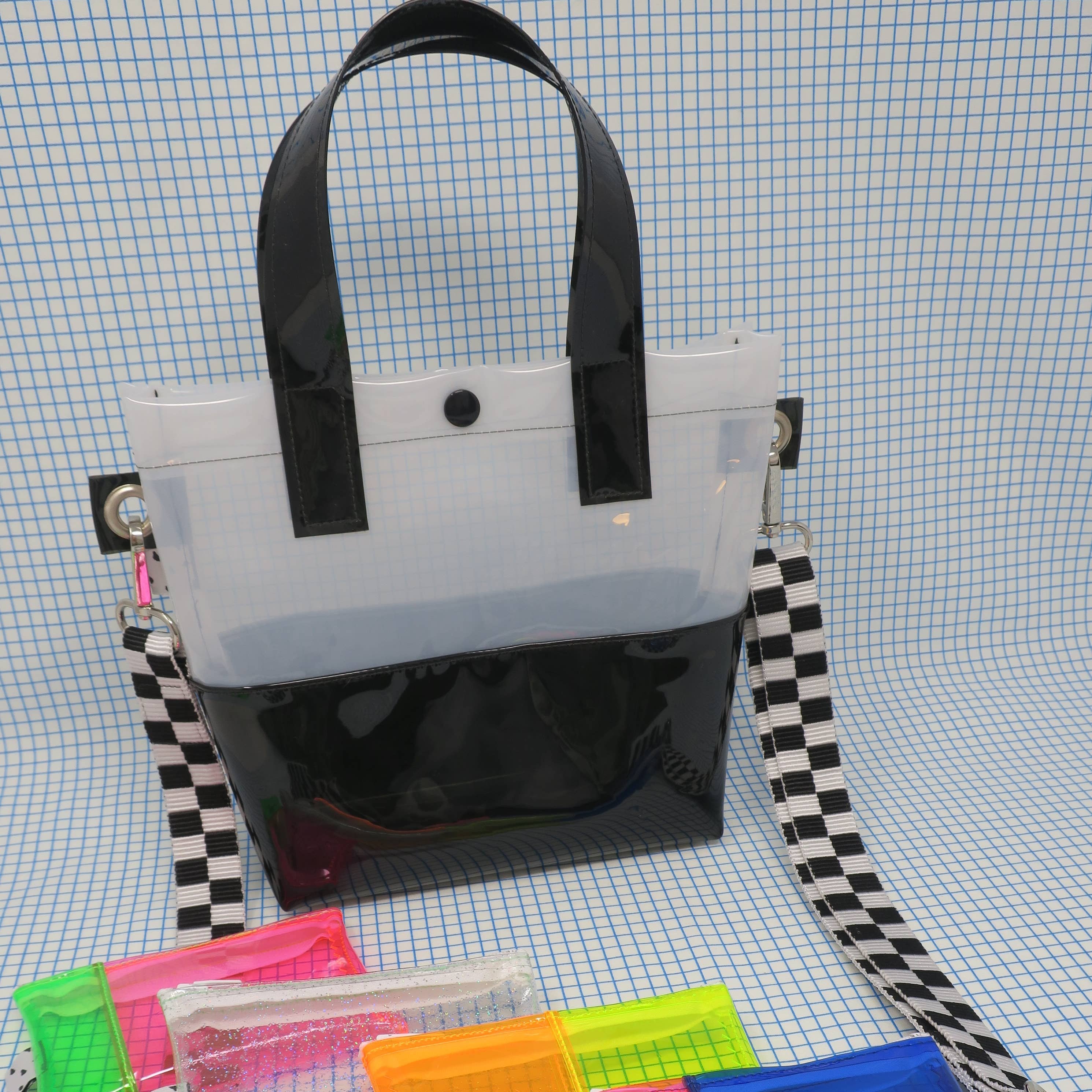 Miss your jelly sandals? This is your new favorite bag! Keep everything inside with a snap. The black and white translucent vinyl handle bag has a black snap closure and is detailed with silver metal grommets. It's available with or without the detachable black and white checkered 1" strap