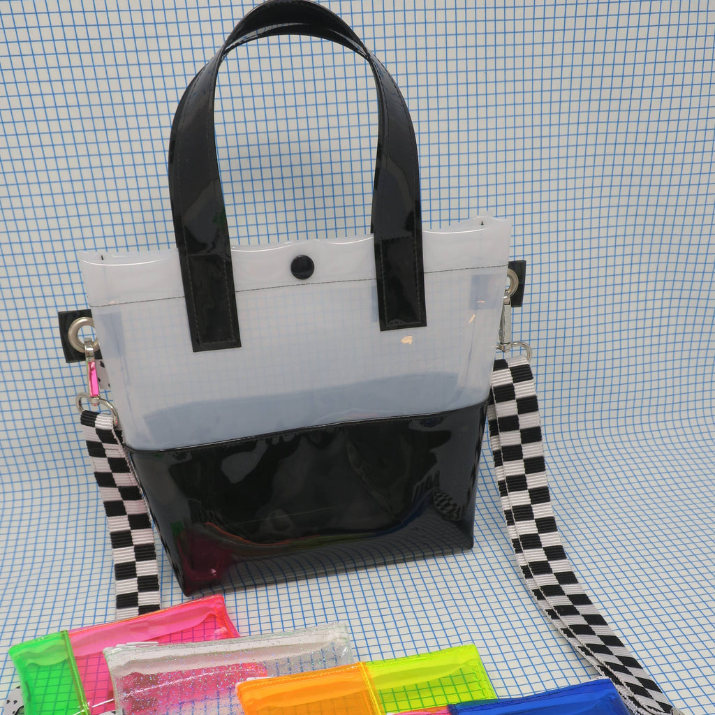 Miss your jelly sandals? This is your new favorite bag! Keep everything inside with a snap. The black and white translucent vinyl handle bag has a black snap closure and is detailed with silver metal grommets. It's available with or without the detachable black and white checkered 1" strap