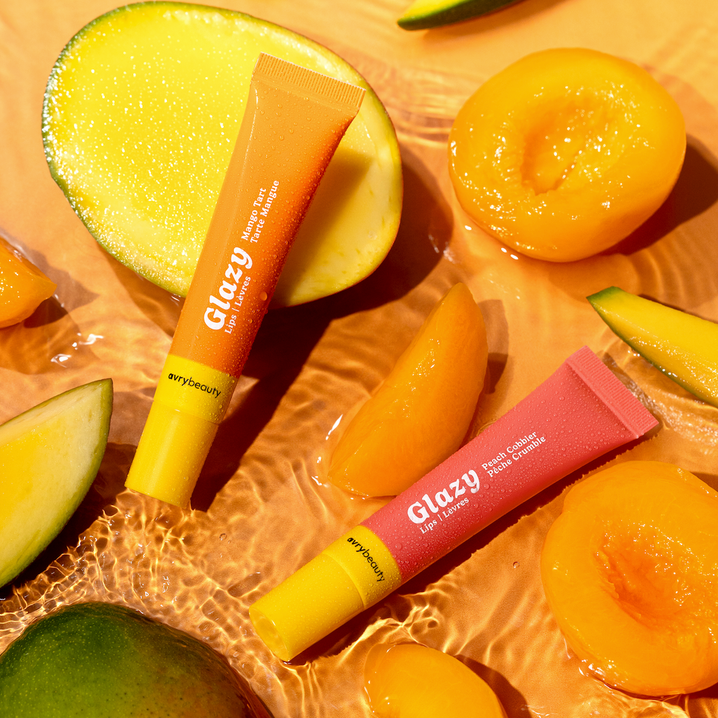 Two Glazy lip balms on a background of sliced mangoes and apricots.