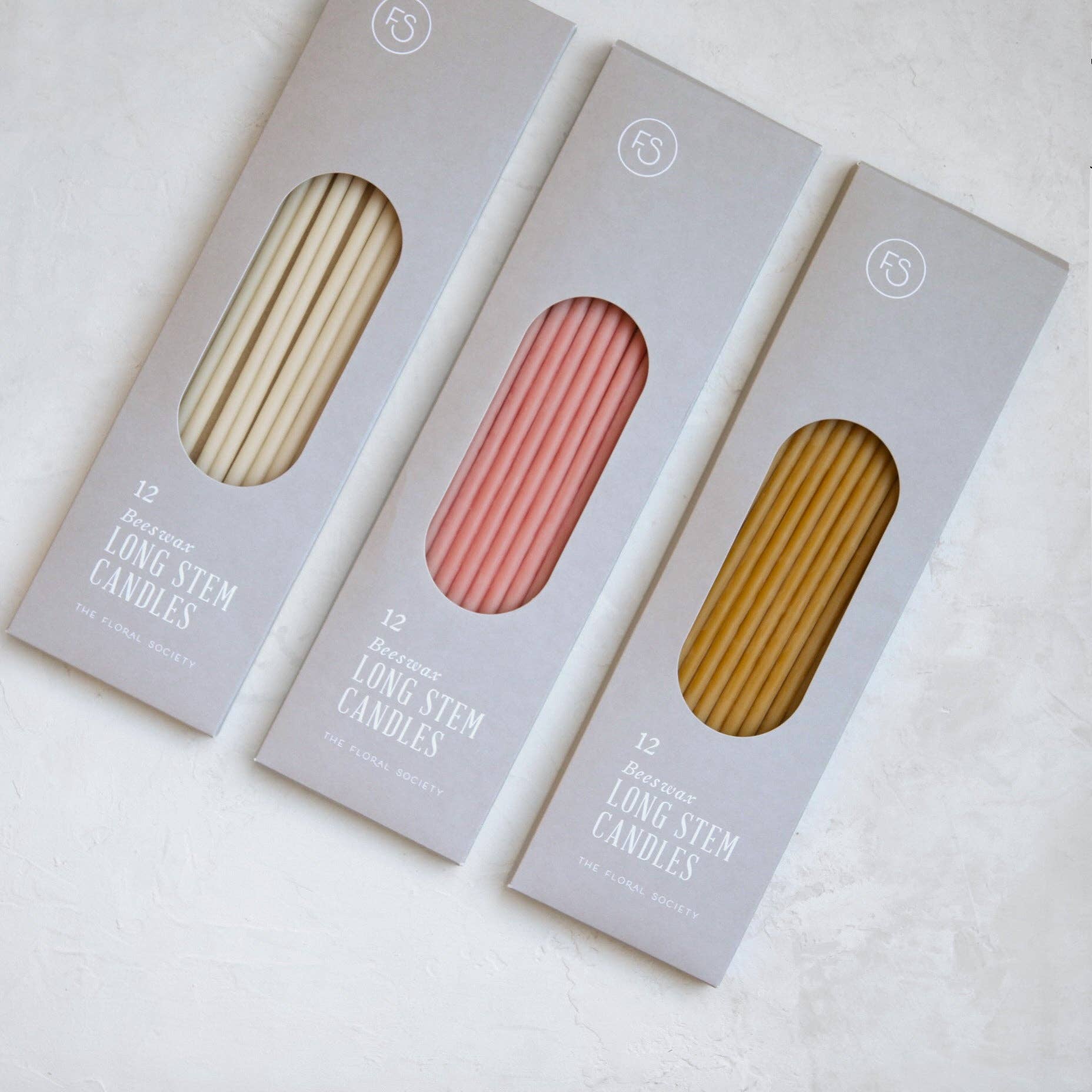 Three boxes of long stem candles in different colors on a white background