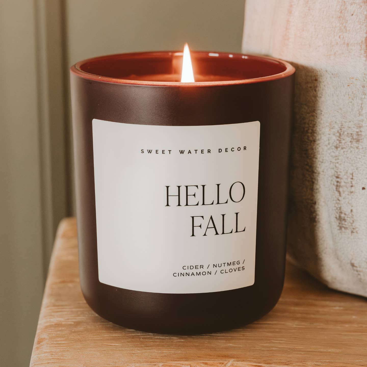 Candle with 'Hello Fall' label on a wooden surface