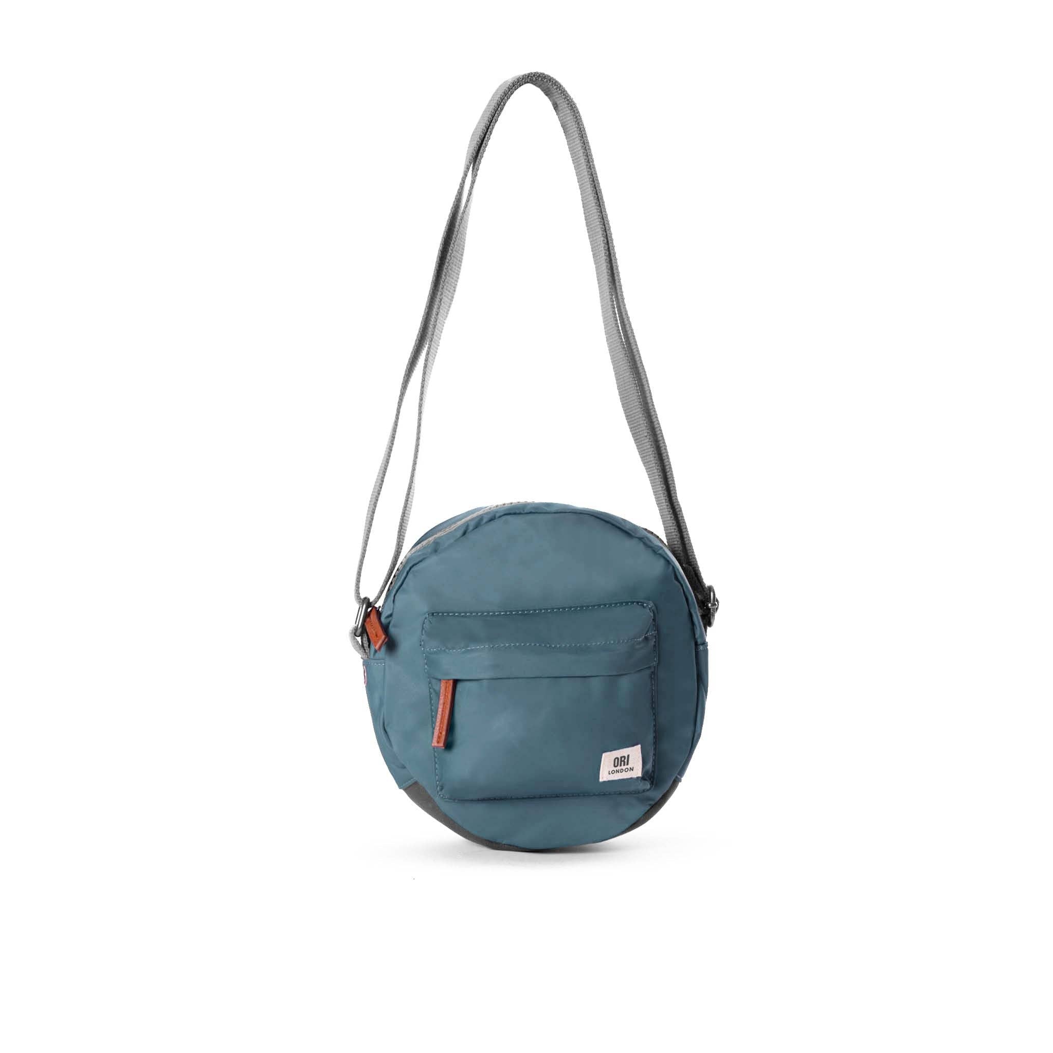 Over the shoulder and crosstown, our Paddington Crossbody is the perfect round bag to sling across your body and take on your day. Airforce Blue color

The Paddington bag has three pockets and sections to keep everything organized, safe and secure, all in weather-resistant, recycled material.

The size is the perfect accessory to store all your daily necessities - mobile, wallet, keys, and more! Our Paddington Crossbody is the only, stylish round bag out there.
