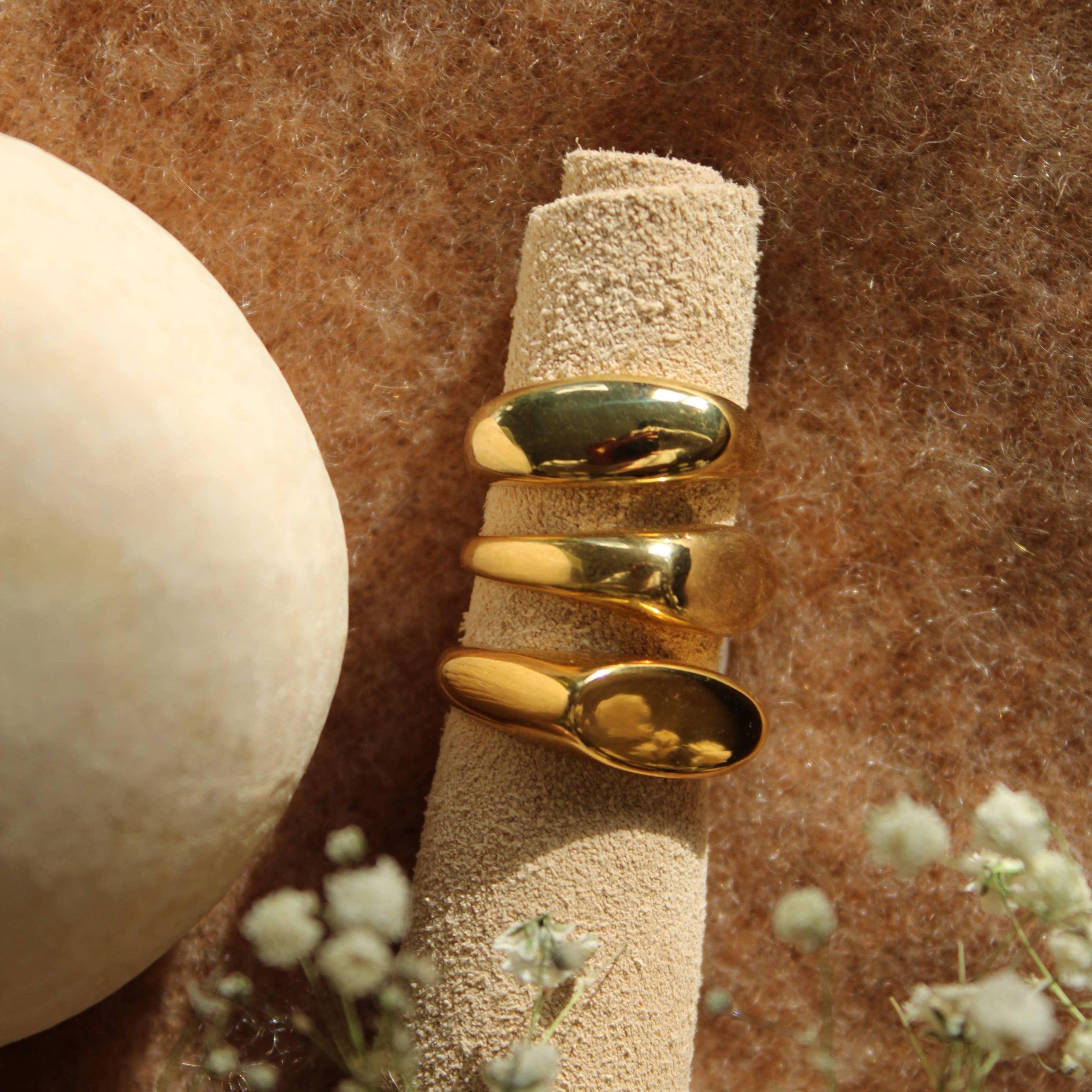 Gold ring on a textured beige surface with flowers in the foreground