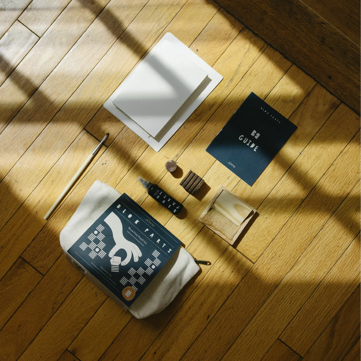 A styled flat-lay of a book and its accompanying accessories arranged on a wooden floor with dramatic window shadows. 