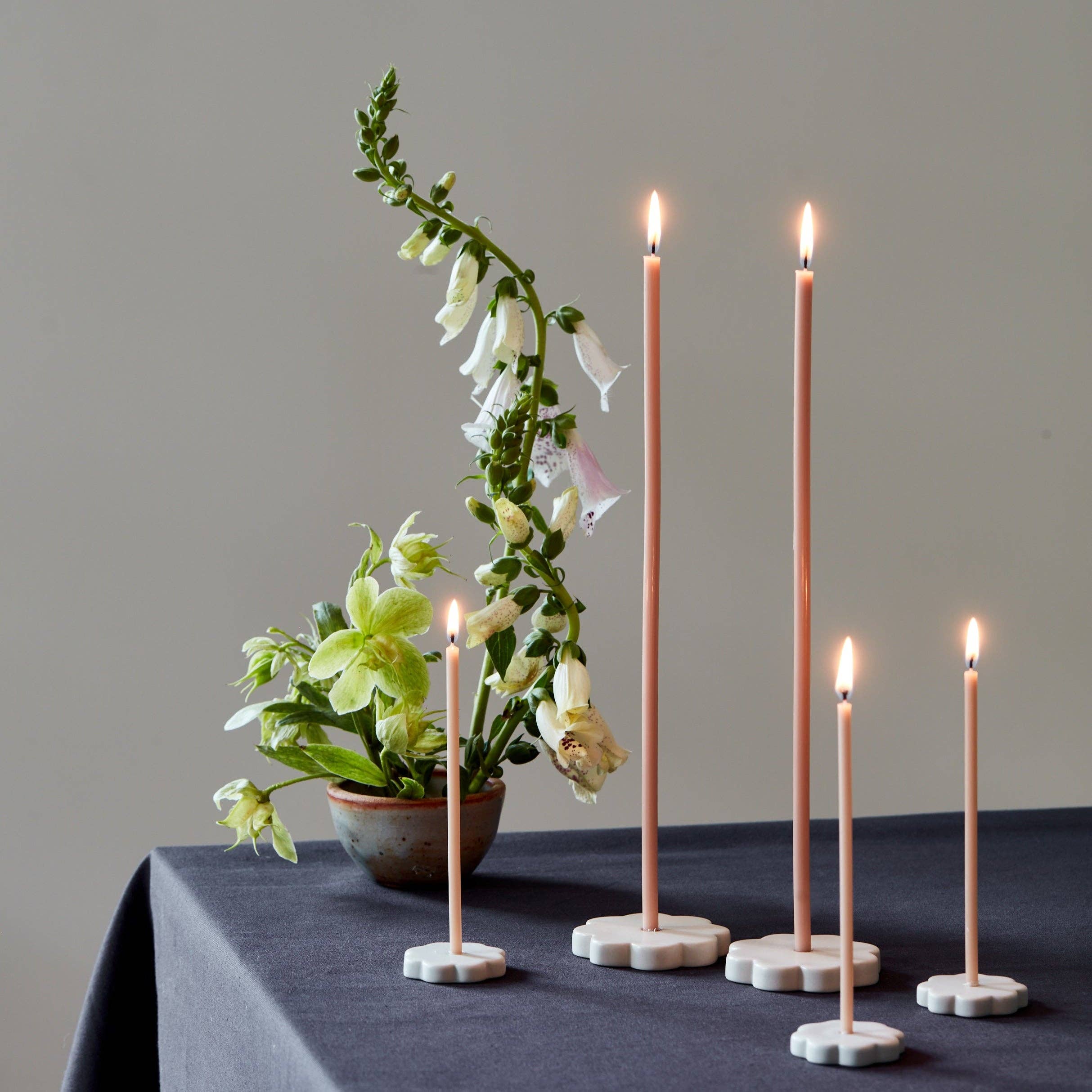 Set of four lit candles on decorative holders with a flower arrangement on a gray background