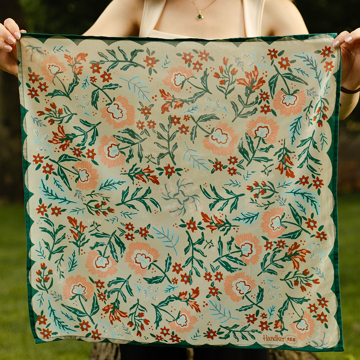 Person holding a floral patterned fabric with green, orange, and white colors.