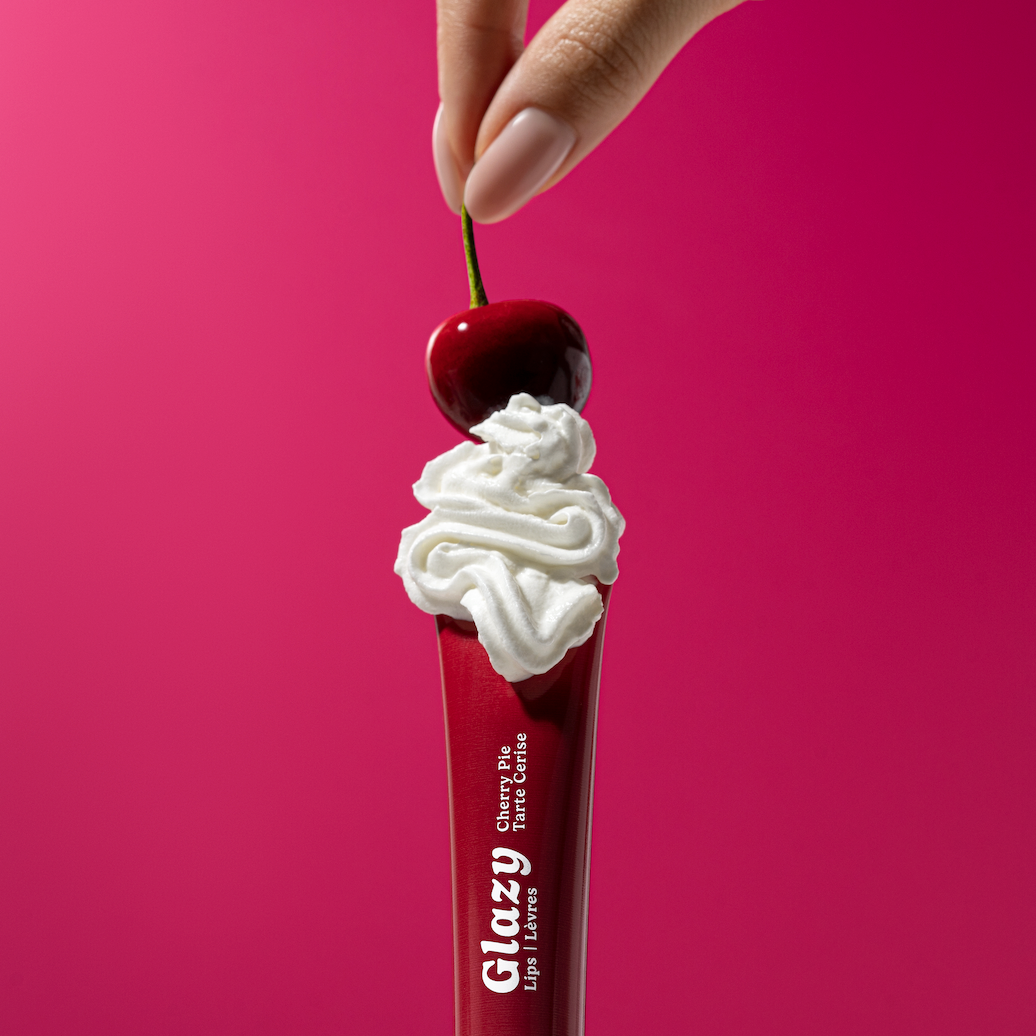 Red Glazy lip balm with whipped cream and a cherry on top against a pink background