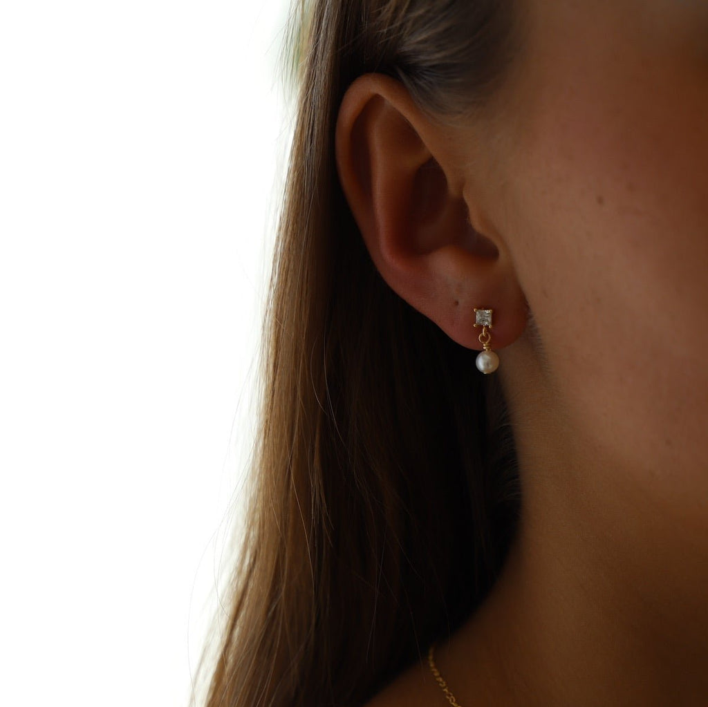 Add a touch of elegance with Claire Pearl Studs. These miniature cz square studs feature a freshwater pearl drop that will elevate any outfit. Perfect for those who love a hint of quirk and sophistication.