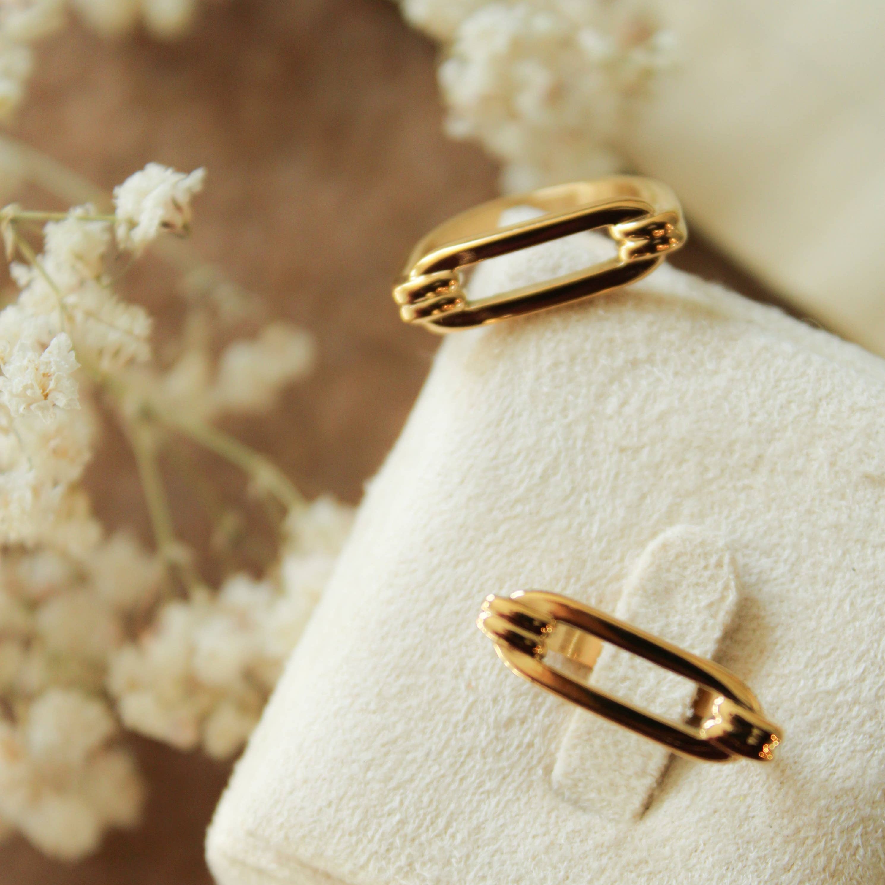 Gold ring on a textured white surface with blurred floral background