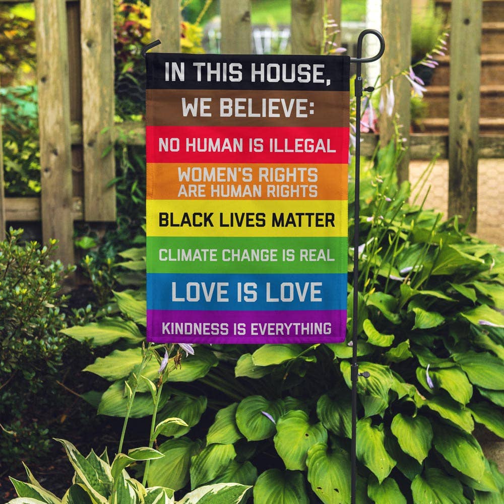 Garden flag with the following text on a rainbow field:

IN THIS HOUSE, WE BELIEVE: NO HUMAN IS ILLEGAL WOMEN'S RIGHTS ARE HUMAN RIGHTS BLACK LIVES MATTER CLIMATE CHANGE IS REAL LOVE IS LOVE KINDNESS IS EVERYTHING These garden flags are a thick double-sided construction and double-stitched all around. They have a pole pocket along the top to fit any standard garden flag stake (not included). 18" x 12"