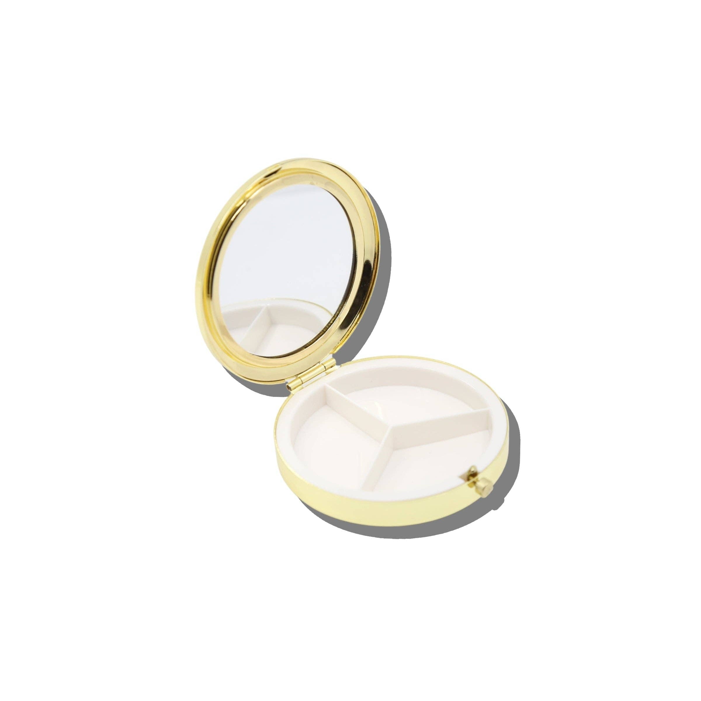 An open round compact case with a gold-tone metal frame and mirror, showing a white interior with three compartments, on a plain white background.