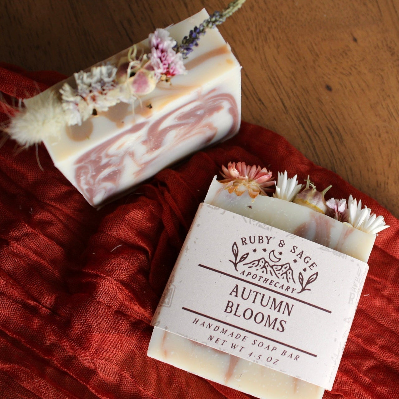 Rectangular handmade soap bar labeled “Autumn Blooms” from Ruby & Sage Apothecary, in soft orange and cream tones, topped with dried flowers and herbs for decoration.