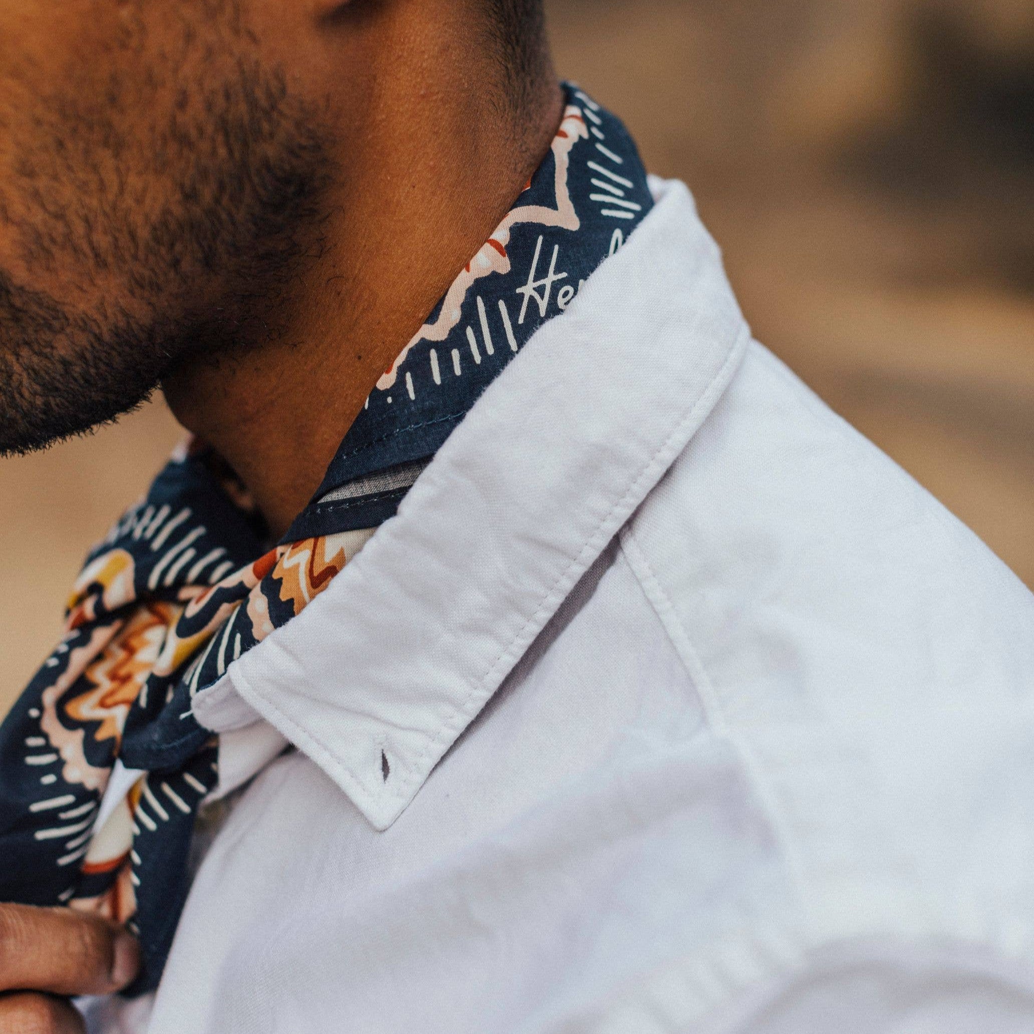Man wearing a patterned scarf and light-colored shirt with a blurred natural background
