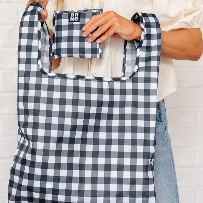 A woman is holding a large black and white checkered reusable shopping bag and a matching small pouch labeled "BRNG."