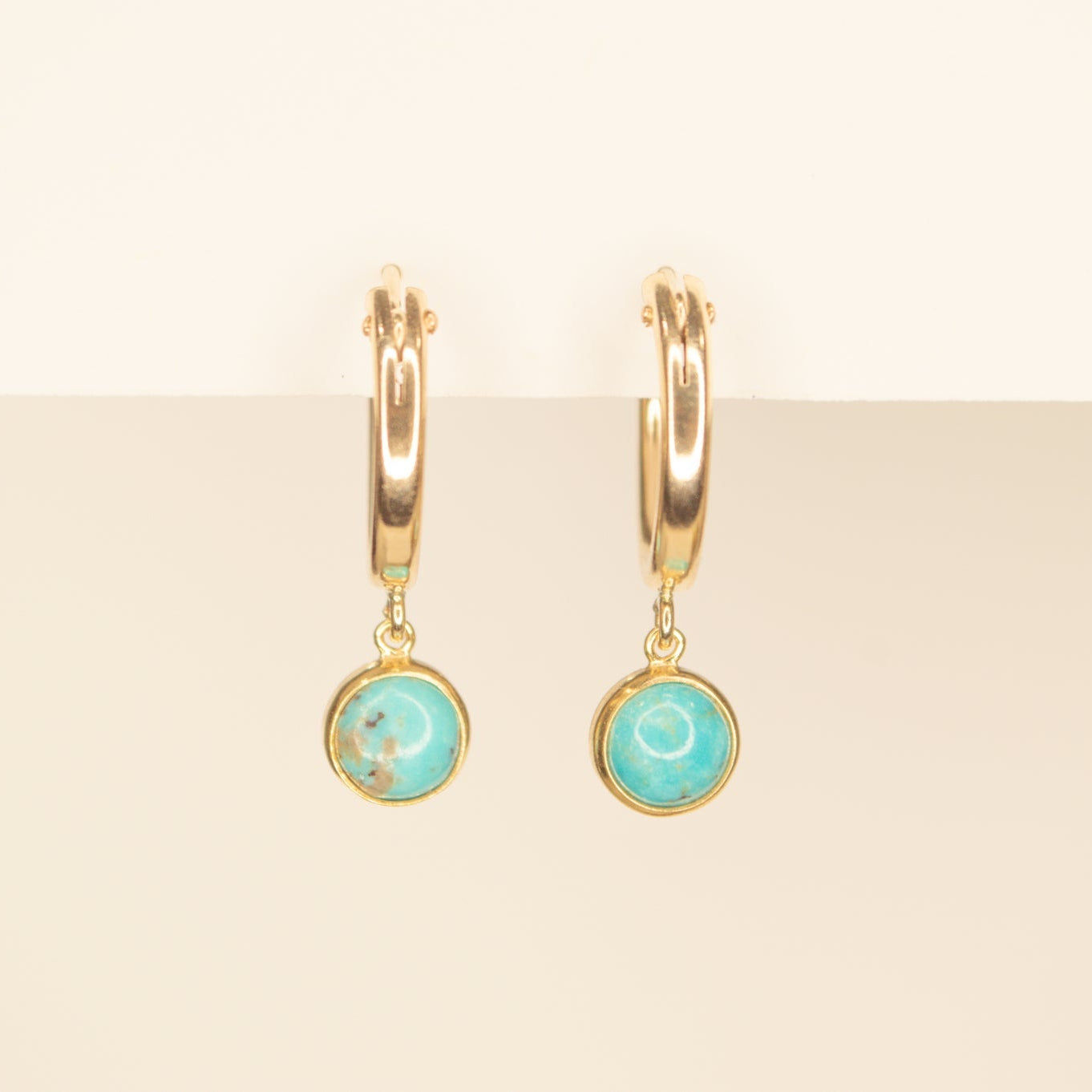 Gold hoops with dainty circle turquiose dangles on a cream back ground.