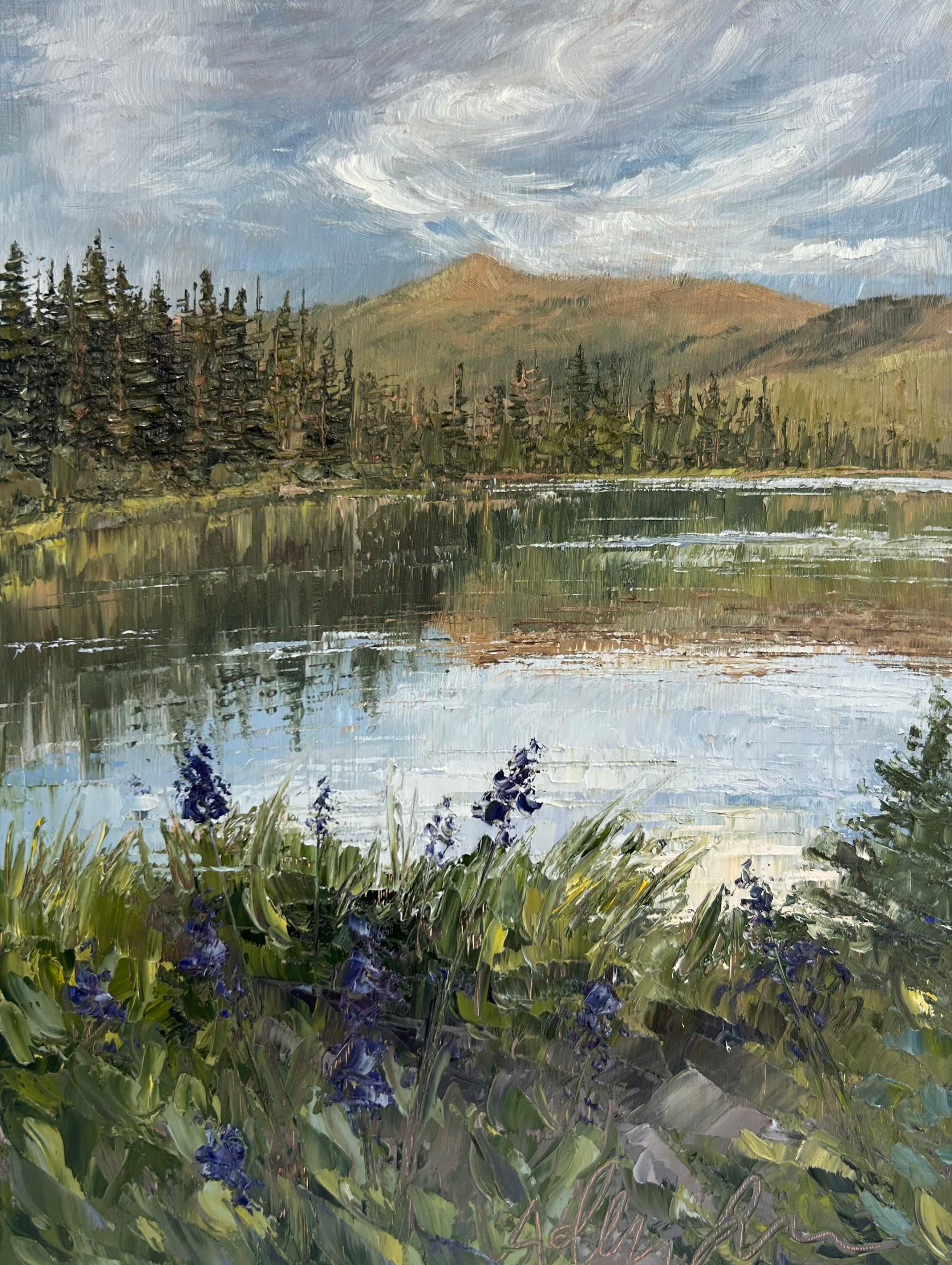 Silver lake surrounded by greenery and a blue, partly cloudy sky. 